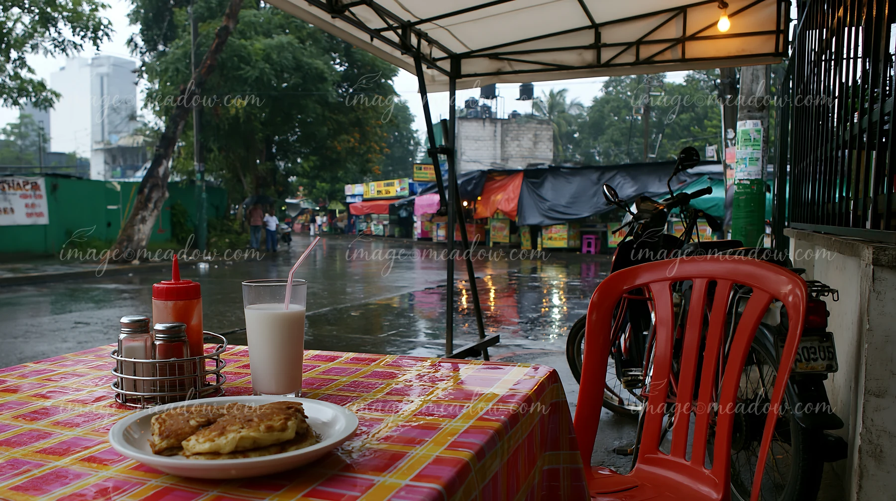 A table set for breakfast features pancakes and a glass of milk, while rain falls outside.