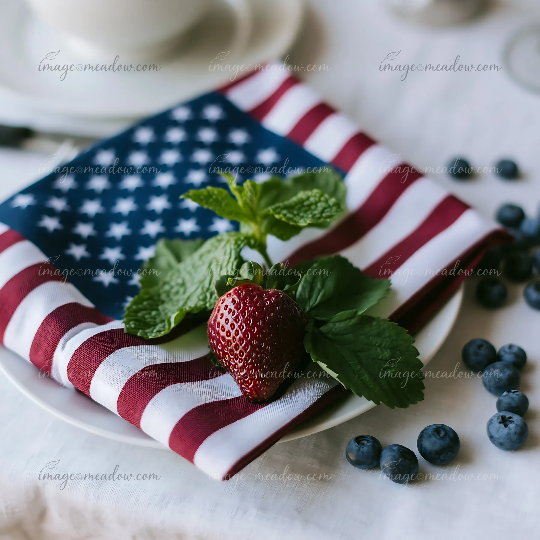 A table setting features an American flag table decoration with a napkin, fresh strawberries, blueberries, and mint leaves arranged on a white plate, creating a