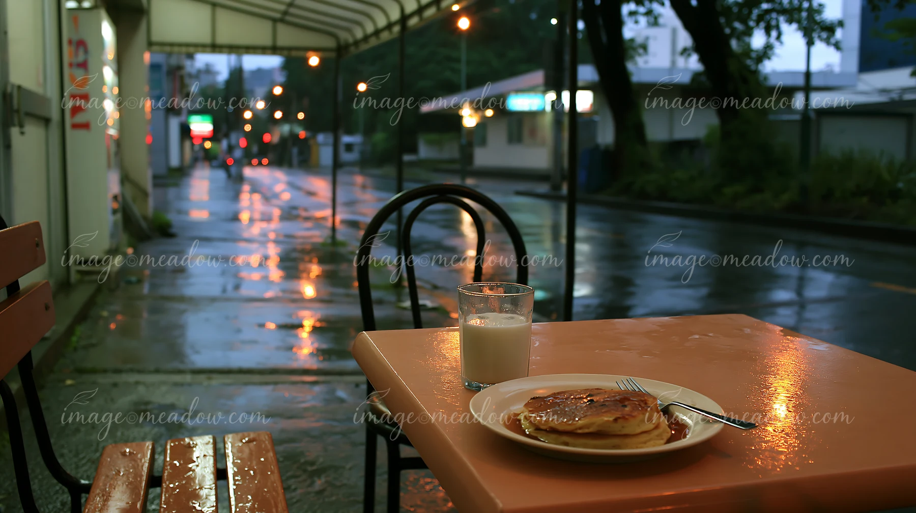 A table sits under a canopy on a rainy street.