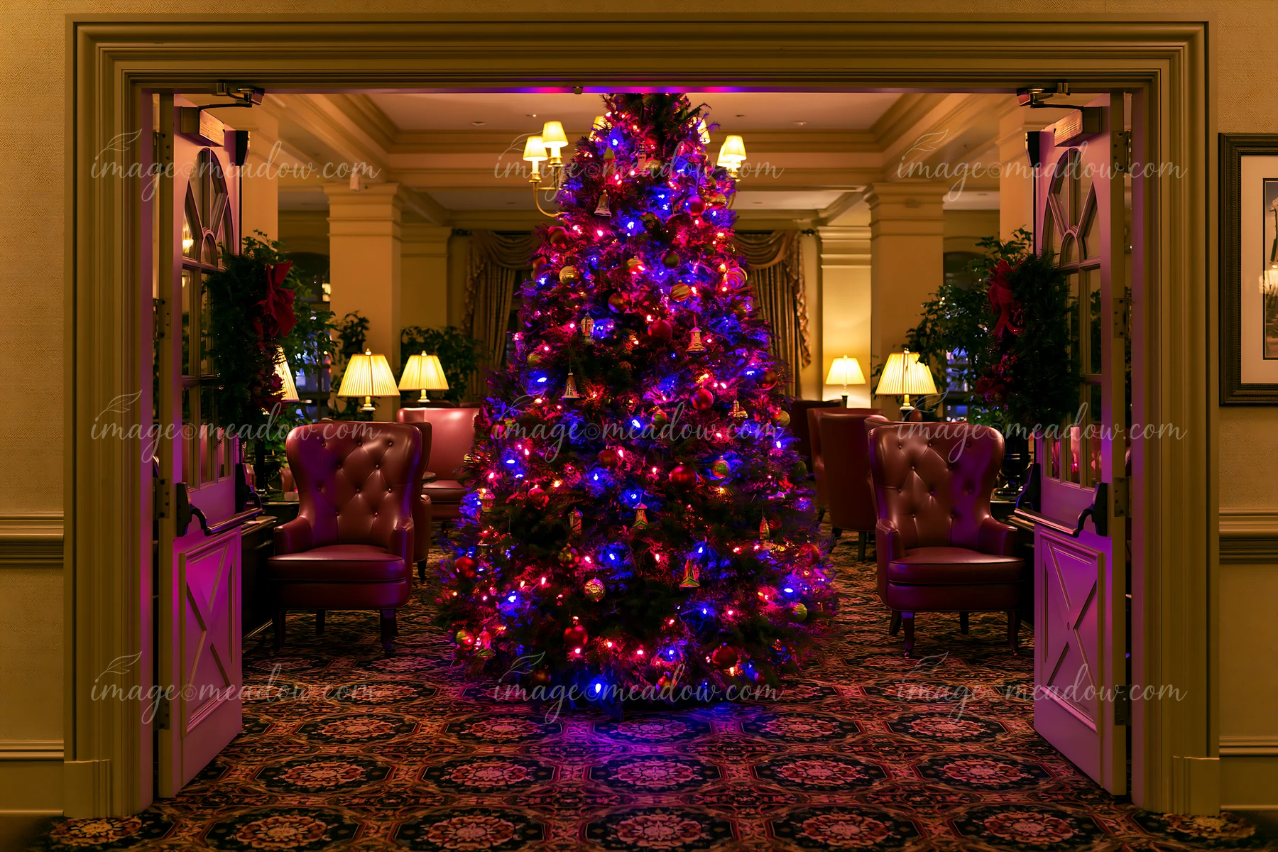 A tall Christmas tree in hotel lobby is decorated with colorful lights and ornaments.