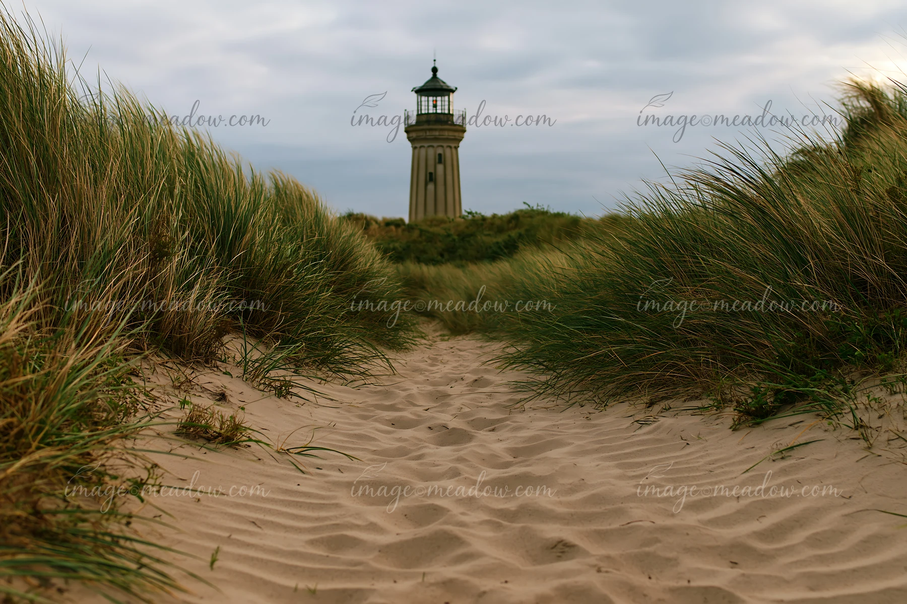 A tall lighthouse stands in the background, surrounded by coastal dunes and tall grass.