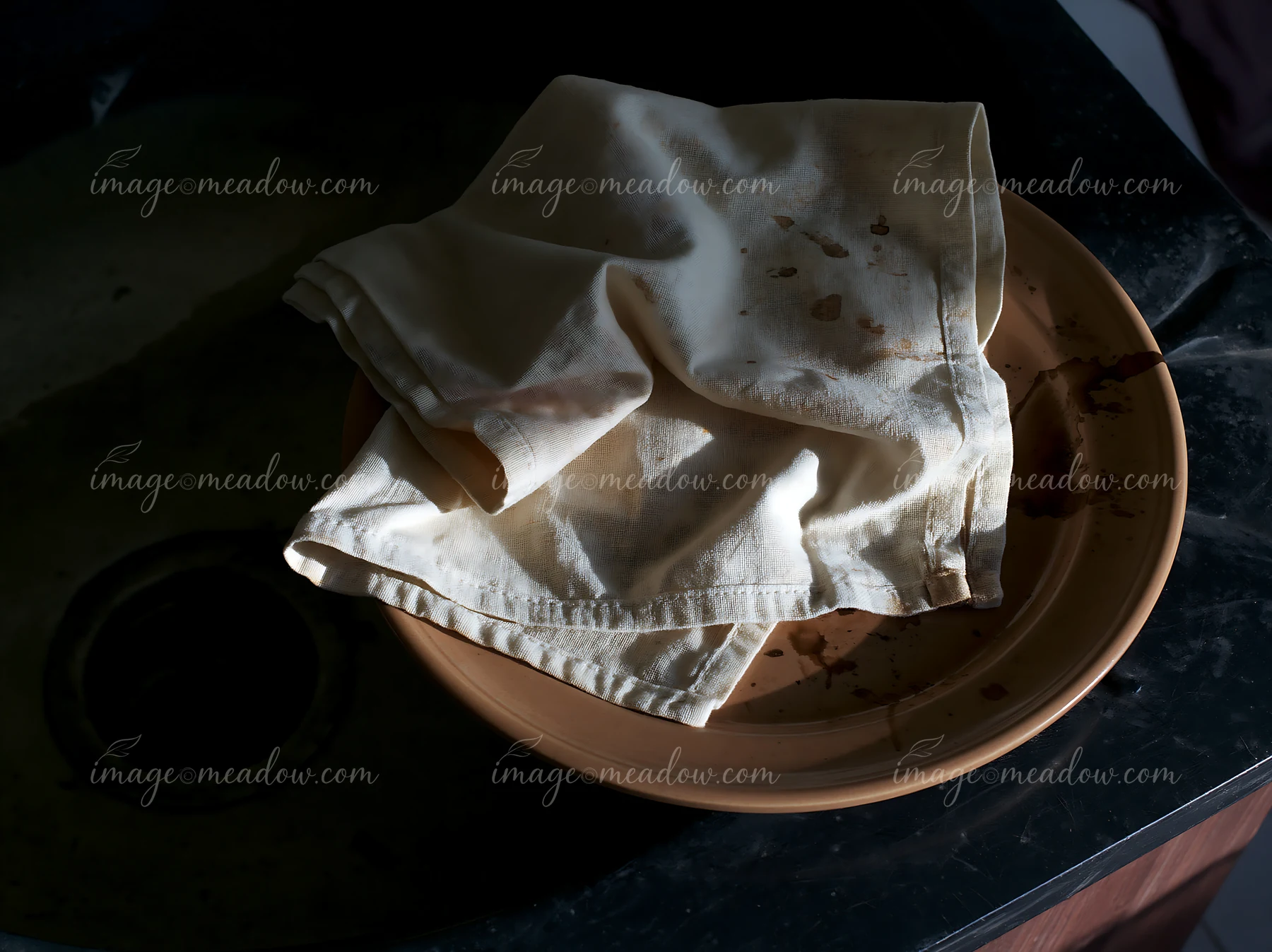 A textile piece with accidental ink splashes rests on a clay dish in a dimly lit setting.