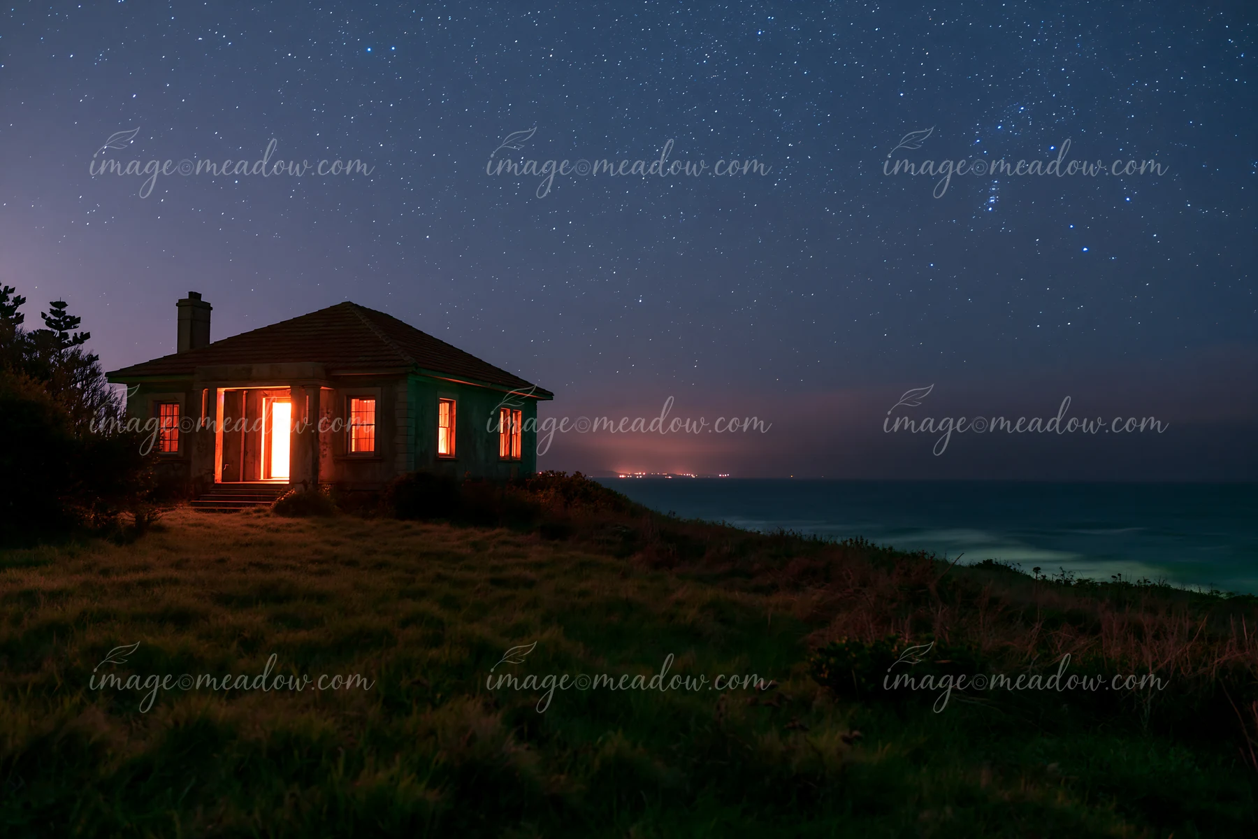 A villa stands on a hillside with lights glowing in the windows under a star-filled sky.