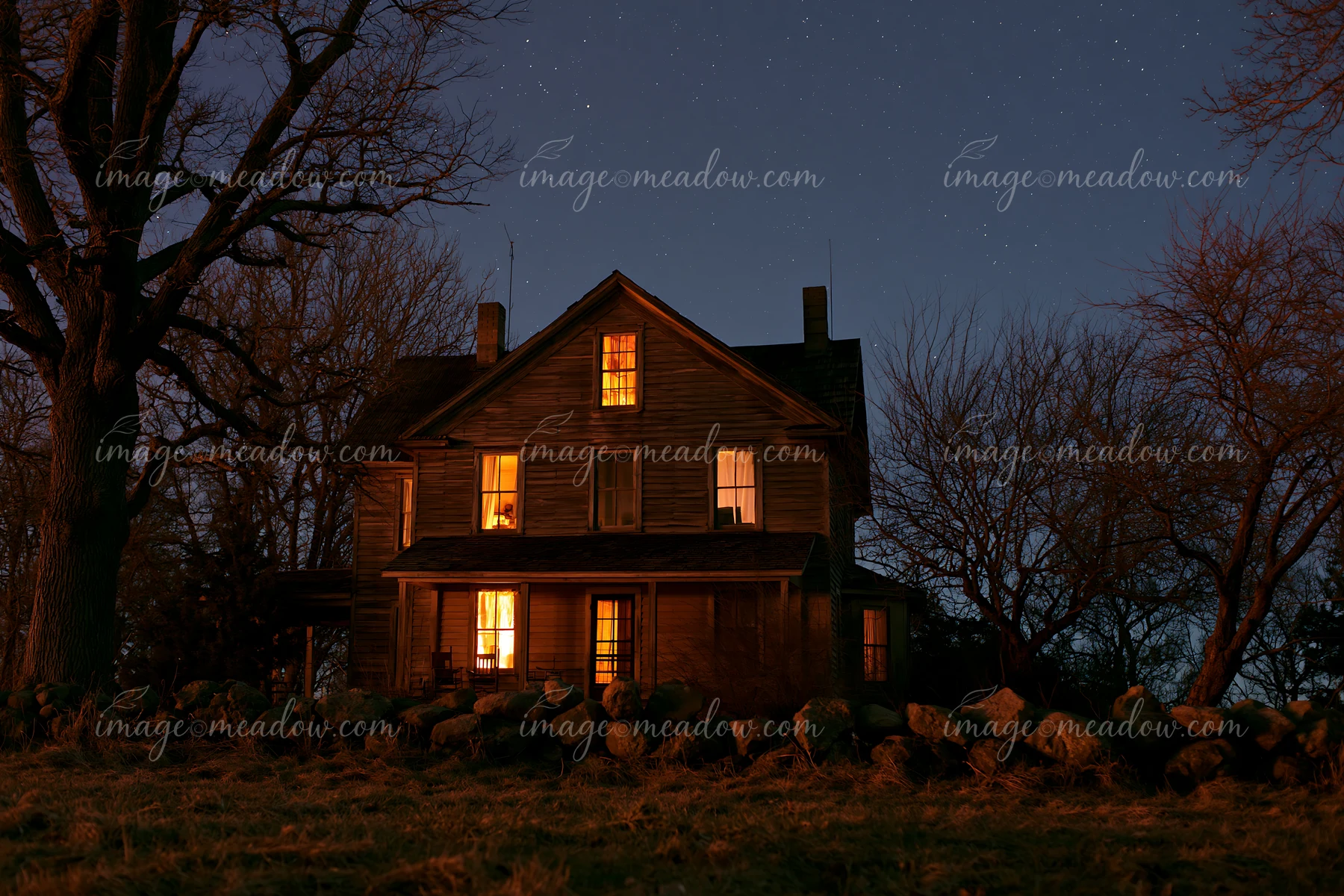 A vintage country house stands in a rural area, with warm lights glowing from its windows against a backdrop of a starry night sky.