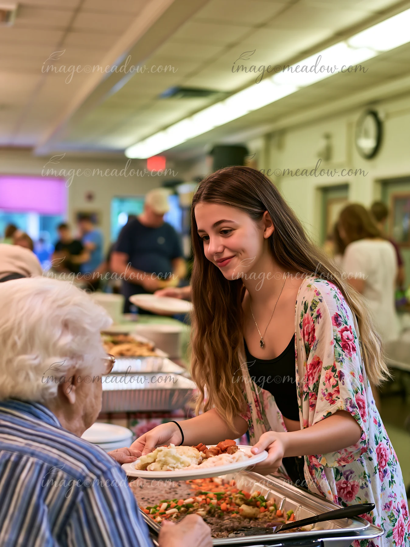 A volunteer serves food at a community potluck buffet, where people gather to share meals and enjoy time together in a community hall.