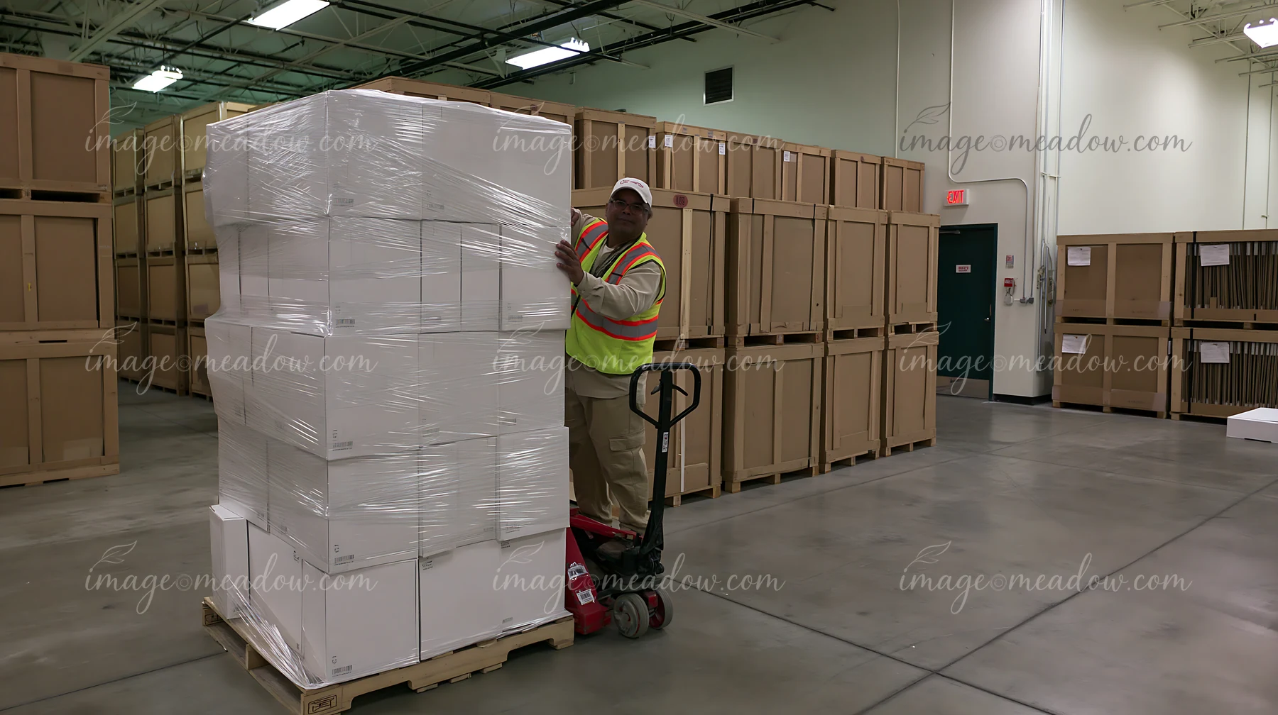 A warehouse worker moves stacked boxes using a pallet jack in a storage facility.