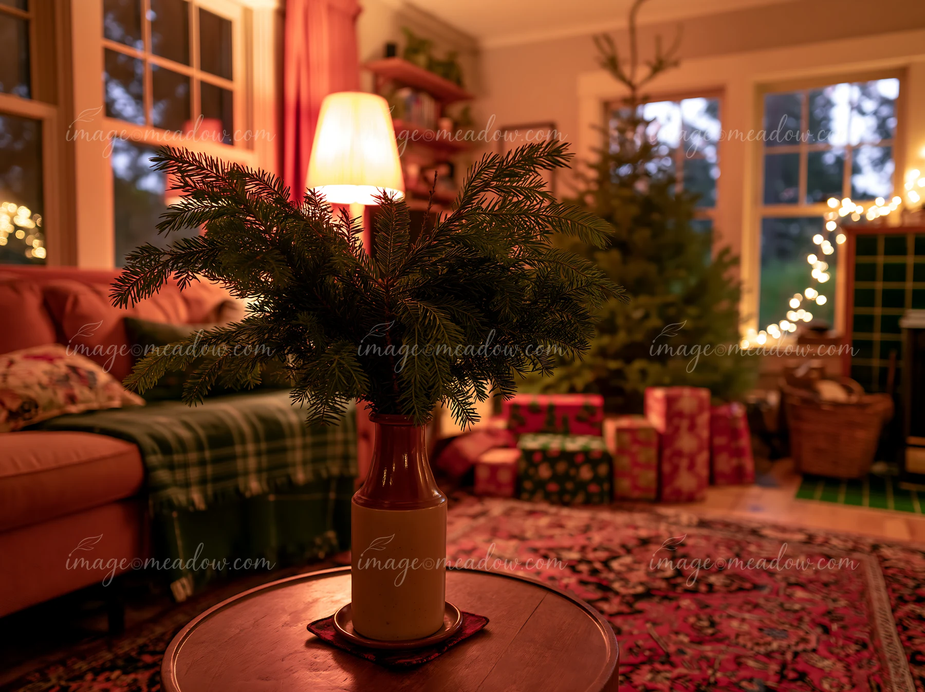 A warm Christmas living room features a small arrangement of natural greenery in a vase, a decorated tree, and wrapped gifts nestled on a colorful rug.
