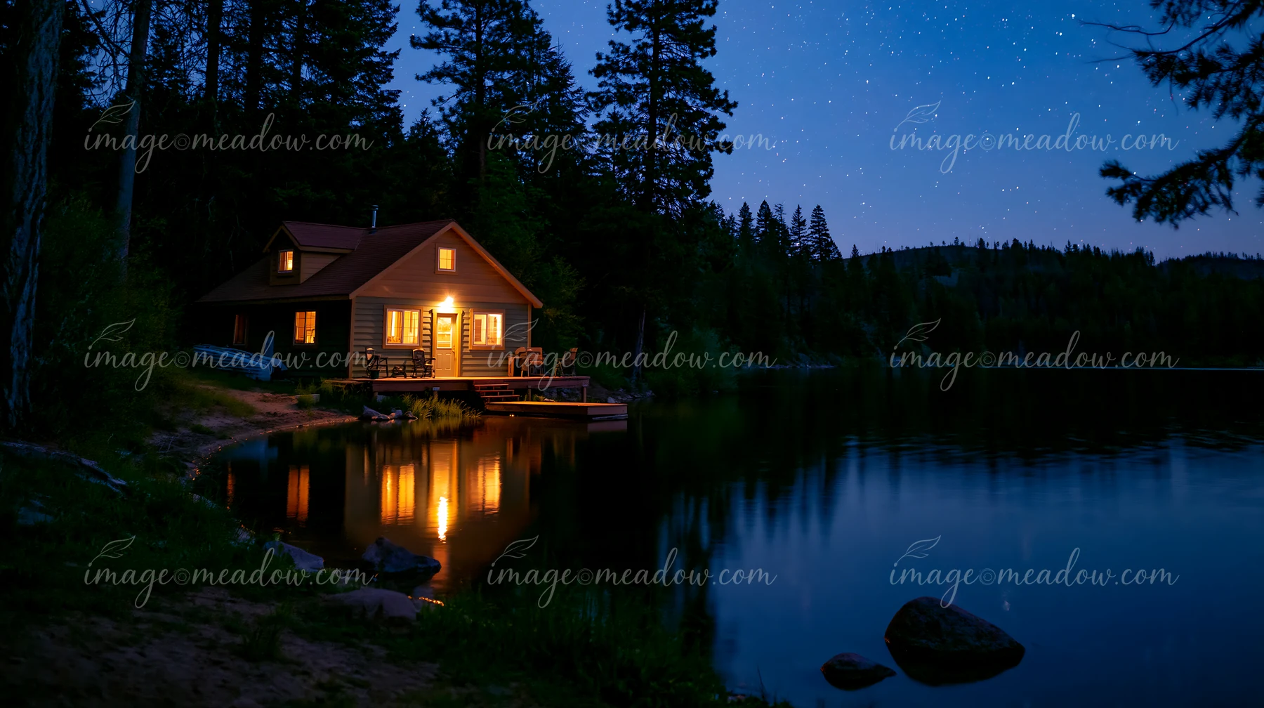 A warm-lit cabin sits beside a calm lake, surrounded by tall trees under a clear night sky full of stars.