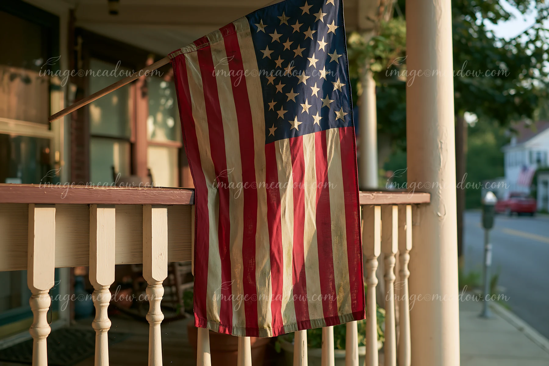A weathered American flag hangs from a porch railing under warm sunlight.