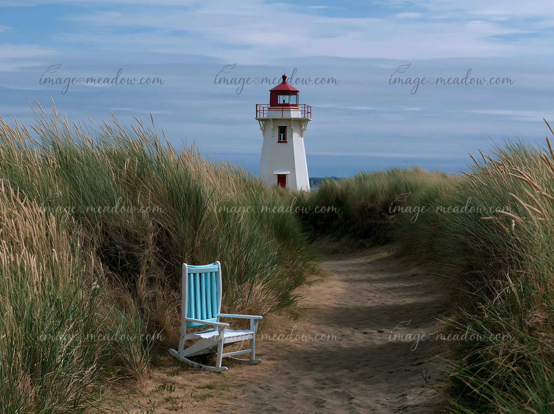 A white lighthouse stands tall amid coastal dunes with tall grass, while a blue chair is positioned along a sandy path leading towards the structure.