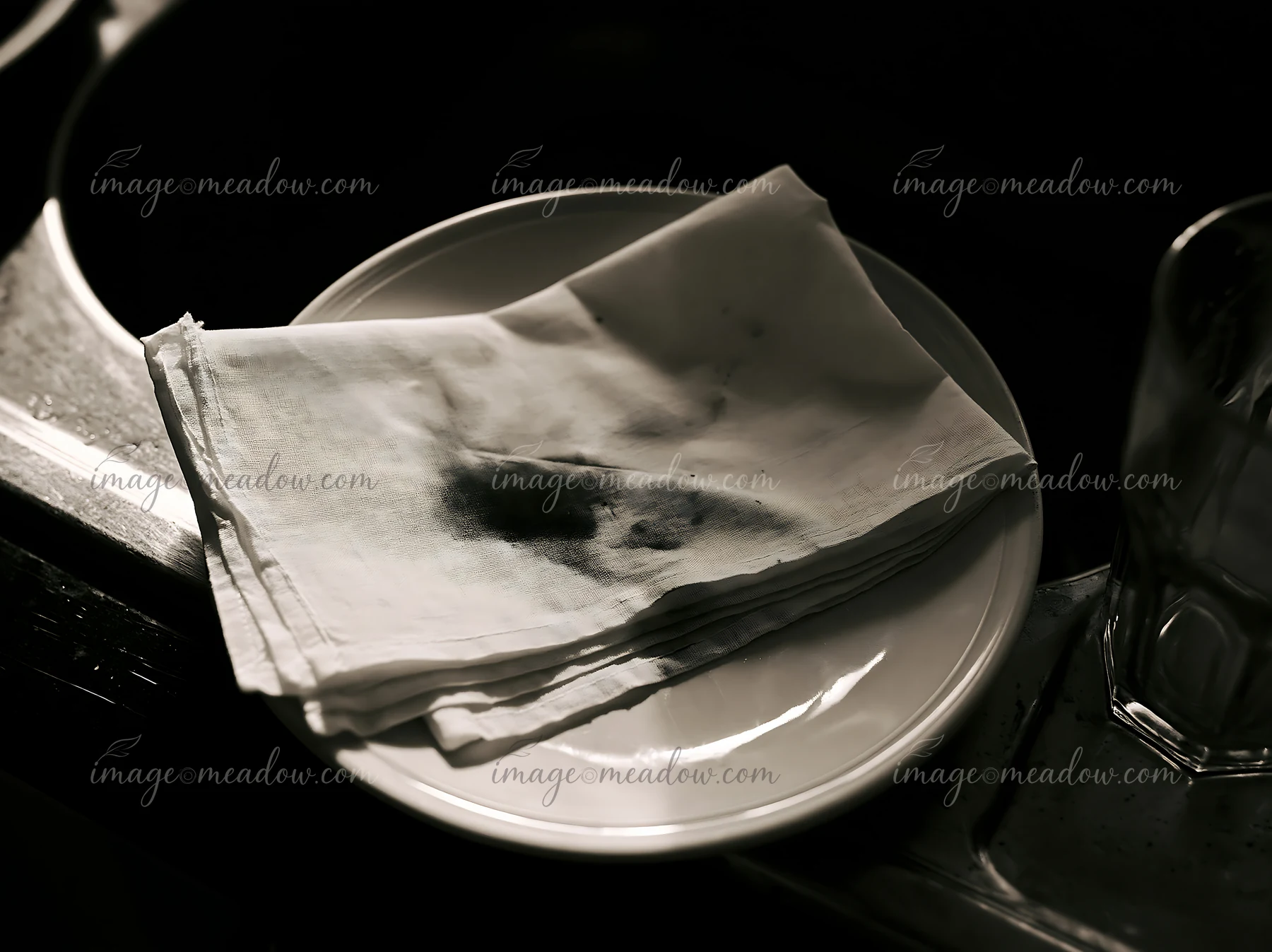 A white textile rests on a plate with visible ink splashes, suggesting a moment of mishap in a dining or crafting setting.