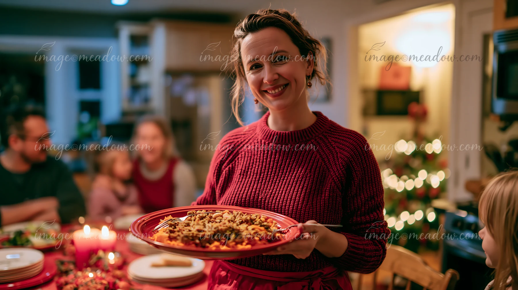 A woman holding a plate of food smiles while standing at a holiday dinner table.