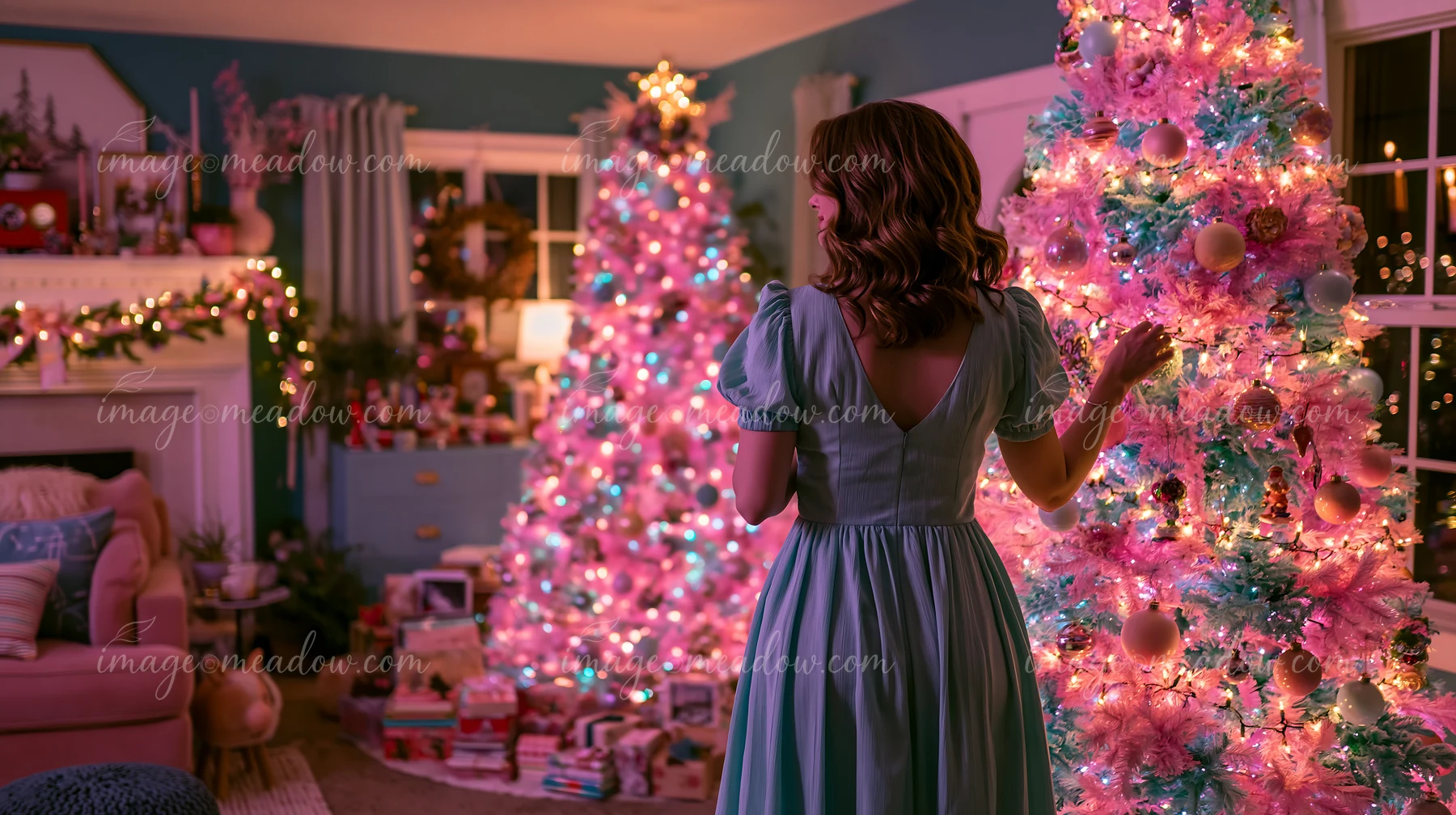 A woman in a blue dress stands in a living room decorated for Christmas with pastel decorations and two colorful trees.