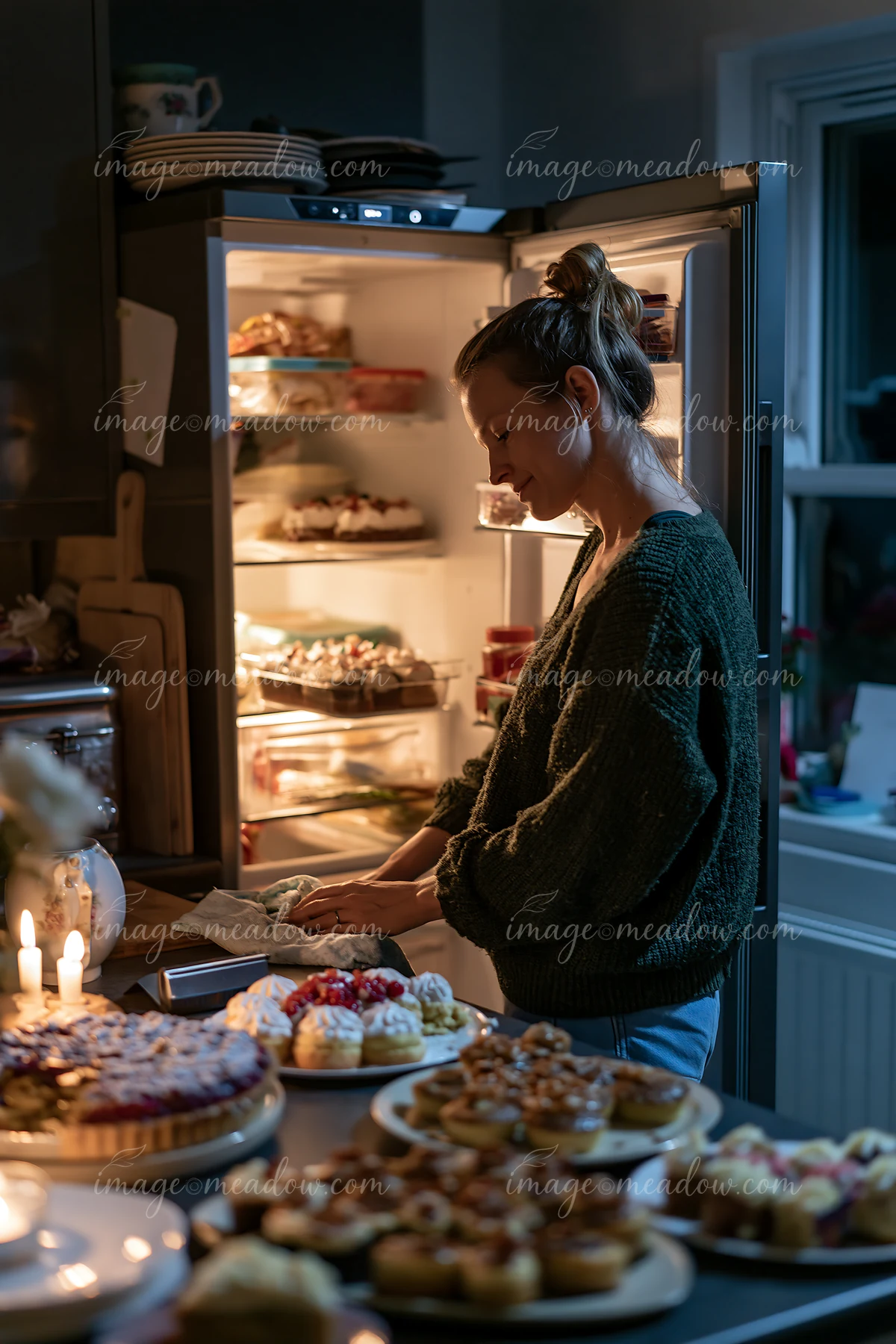 A woman organizes plates of desserts in a kitchen after a festive event.