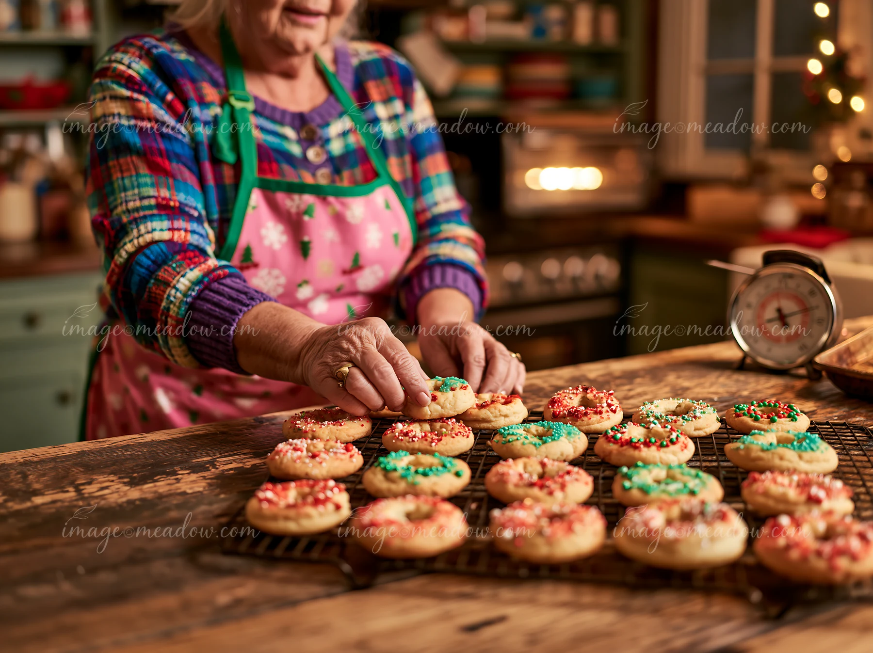A woman places colorful cookies on a kitchen rack to cool after baking.