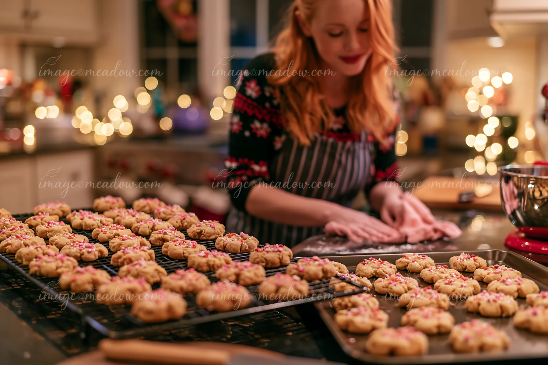 A woman prepares Christmas cookies in a cozy kitchen adorned with warm lights.