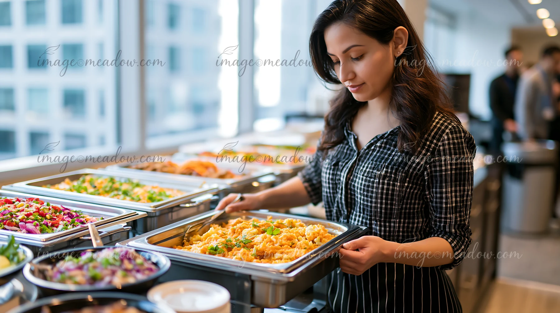 A woman serves food at a corporate lunch buffet set in an office environment.