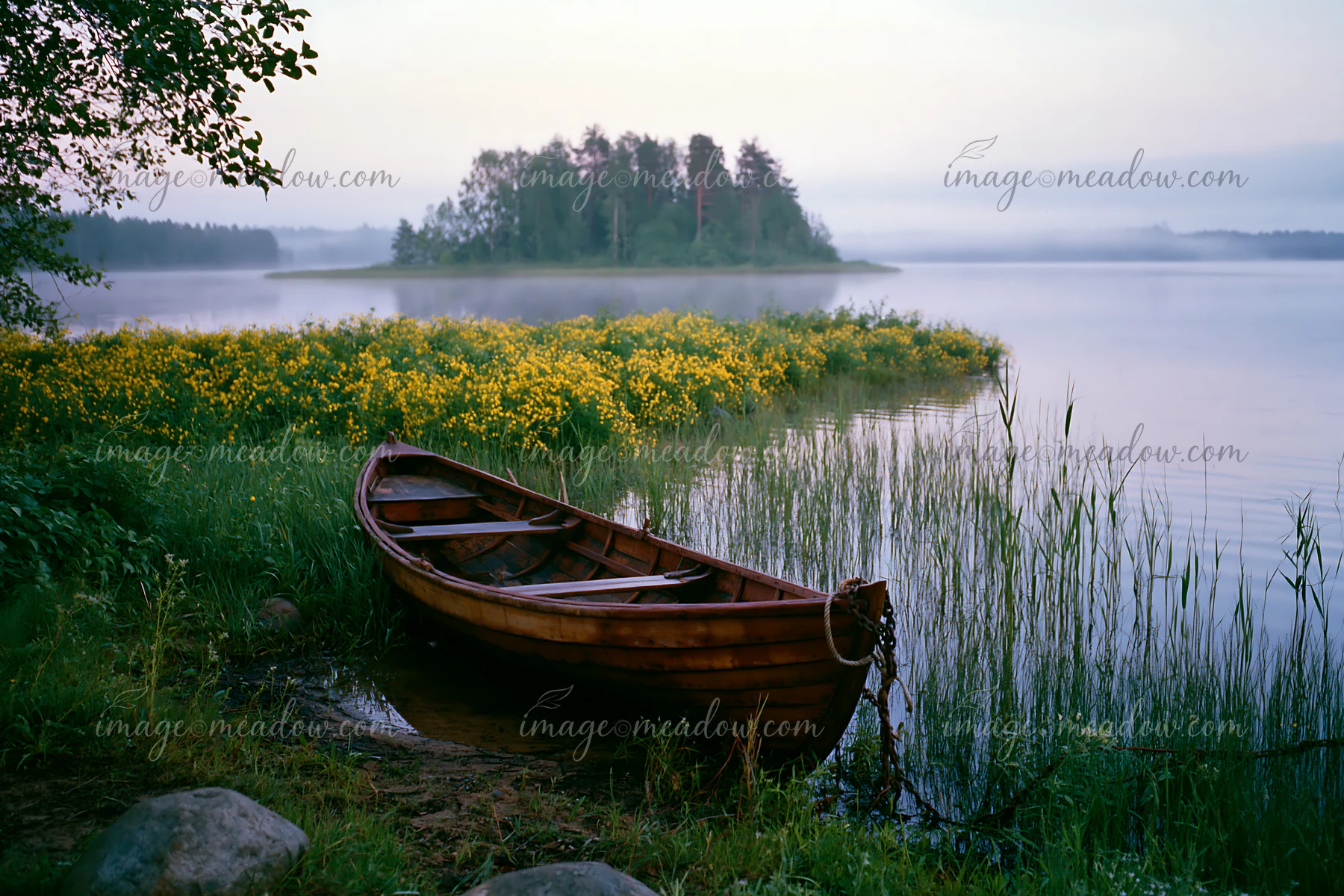 A wooden boat rests on the shore of a lake beside an island covered with buttercups.