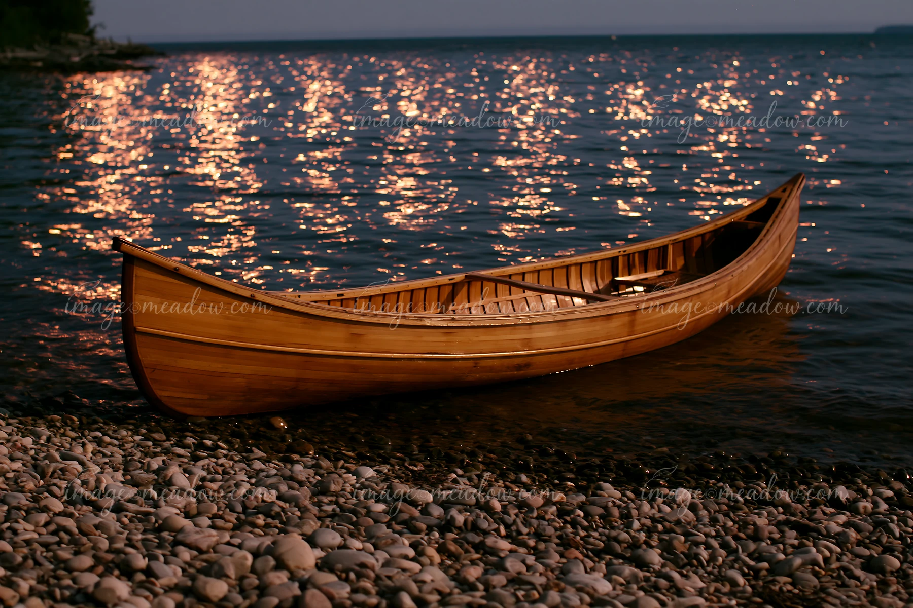 A wooden canoe rests on pebbles along the water's edge.