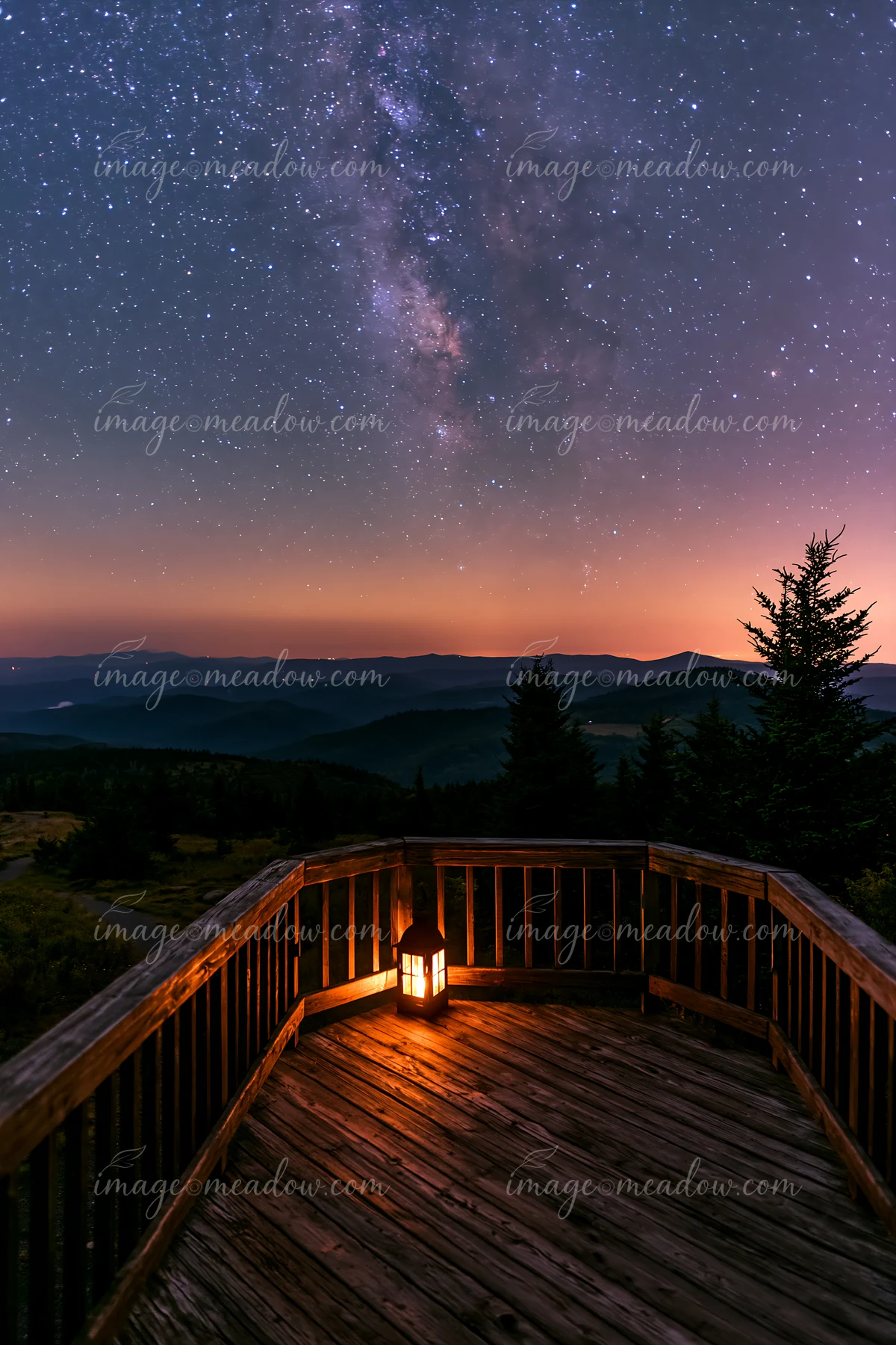 A wooden deck overlooks a mountain valley under a starry night sky.