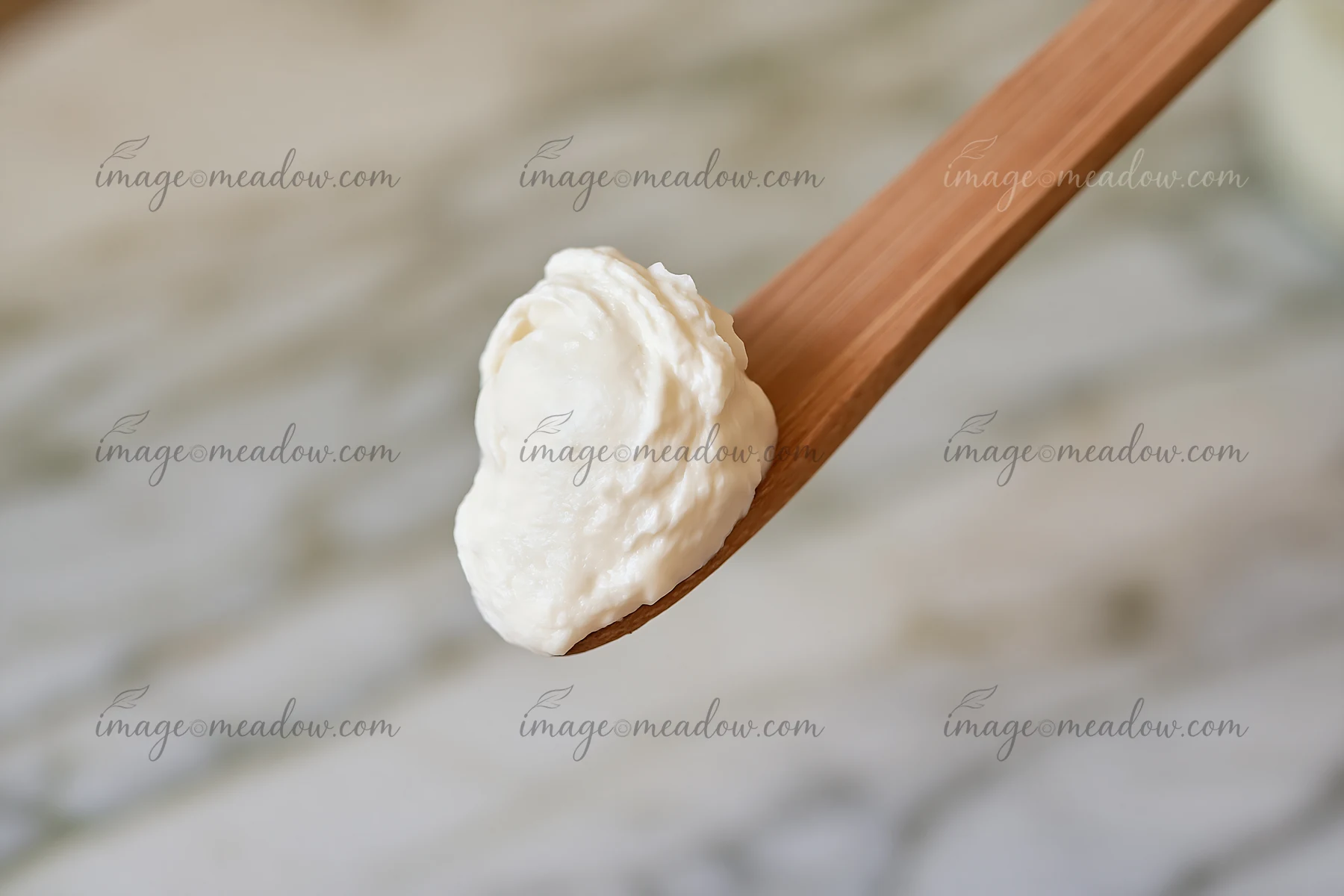 A wooden spoon holds a cream dose with matte texture, placed on a light-colored marble surface.