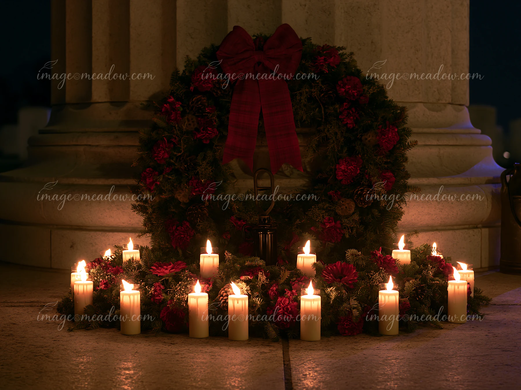 A wreath with red flowers sits at a veterans cemetery under a clear night sky, surrounded by lit candles.