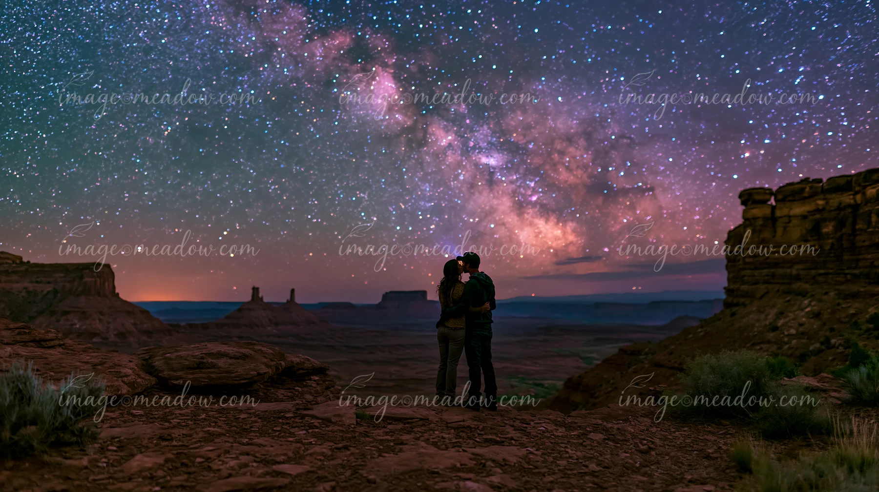 A young couple kissing beneath visible Milky Way in a desert setting during night.