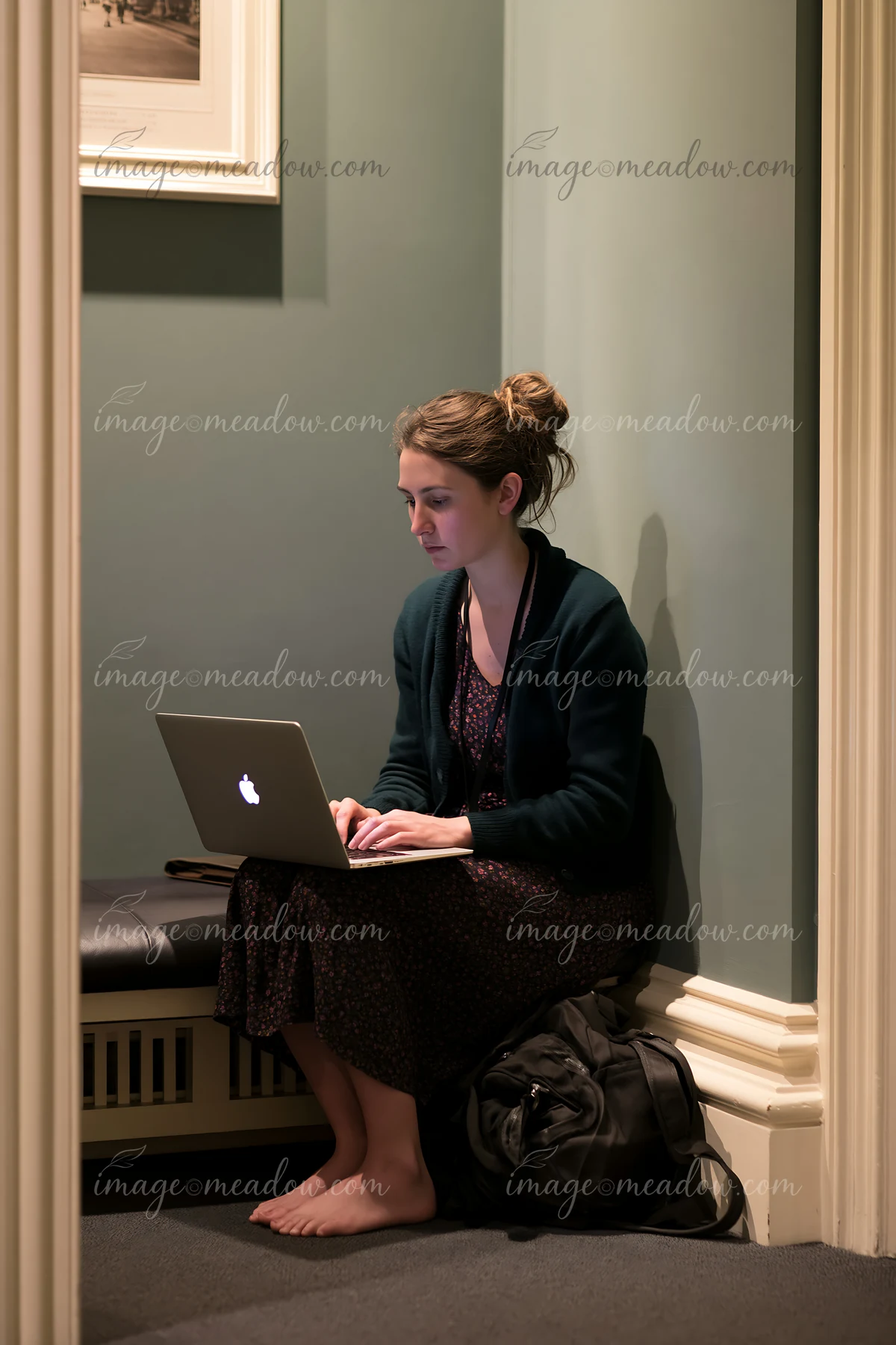 A young woman works on her laptop in a quiet corner of a building.