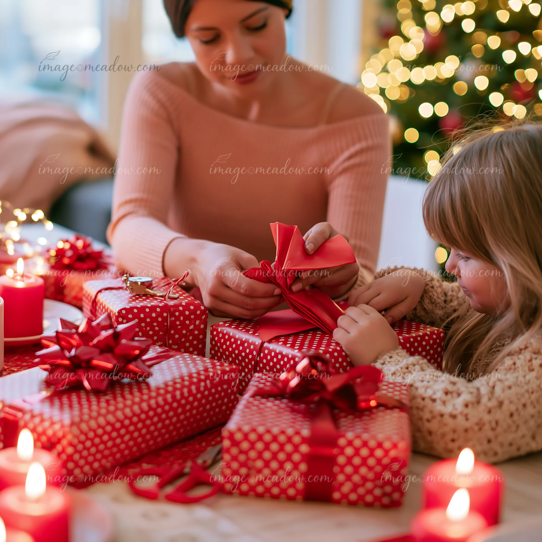 Adult and child tie red ribbon around gifts beside a decorated Christmas tree.