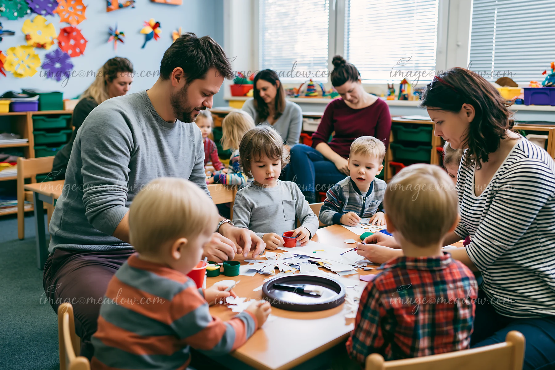 Adults and children make paper snowflakes together at a classroom craft table.