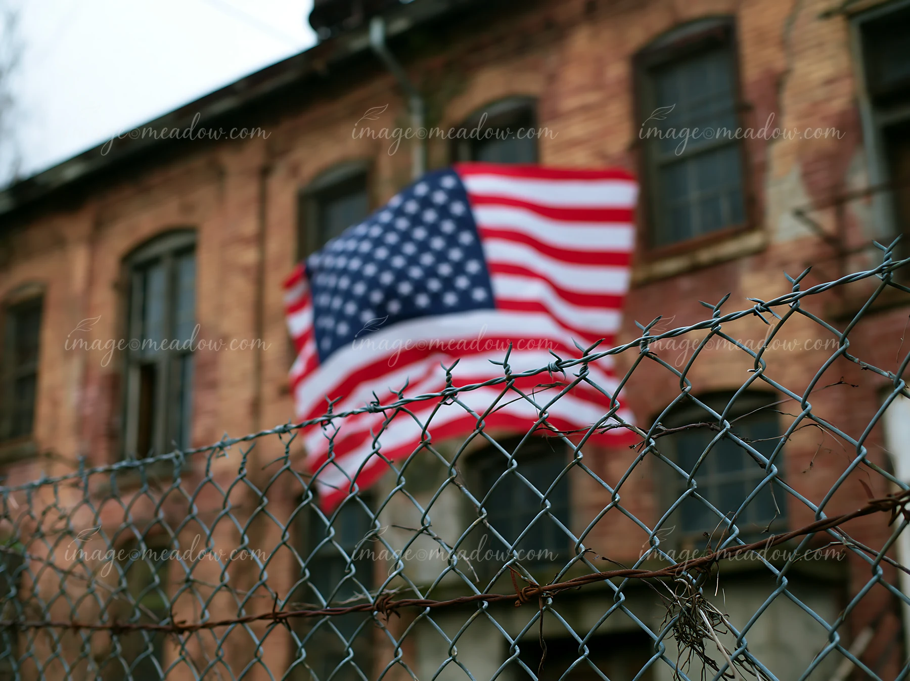 An American flag behind barbed wire flutters near an old building.