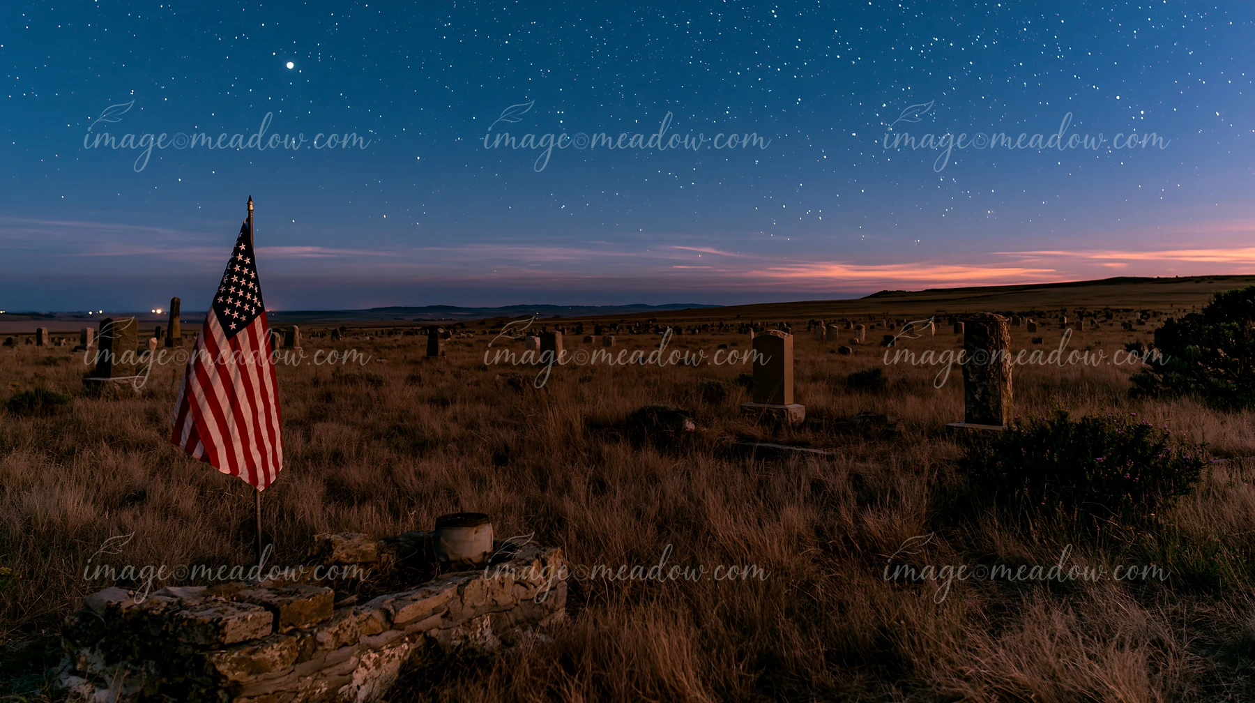 An American flag stands among graves in a cemetery illuminated by stars at night.