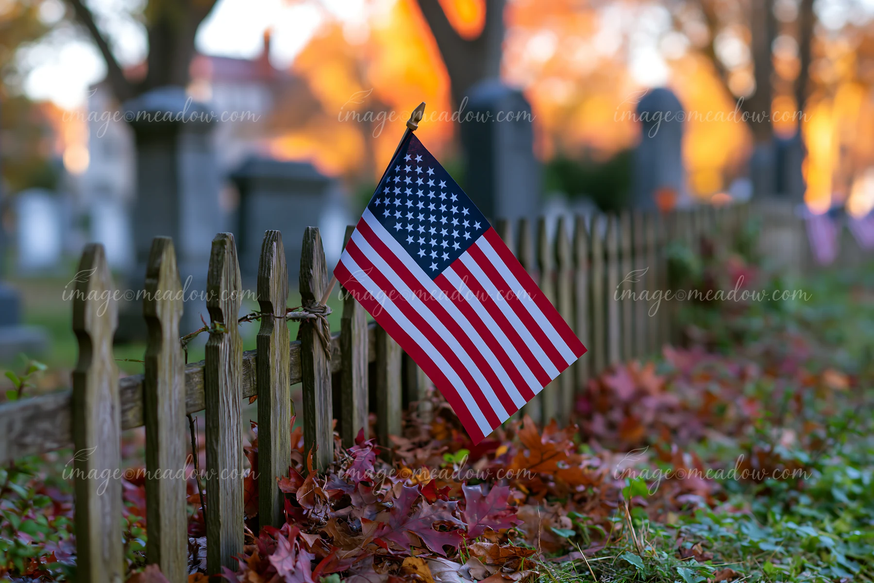 An American flag stands at the edge of Arlington cemetery among fallen leaves.