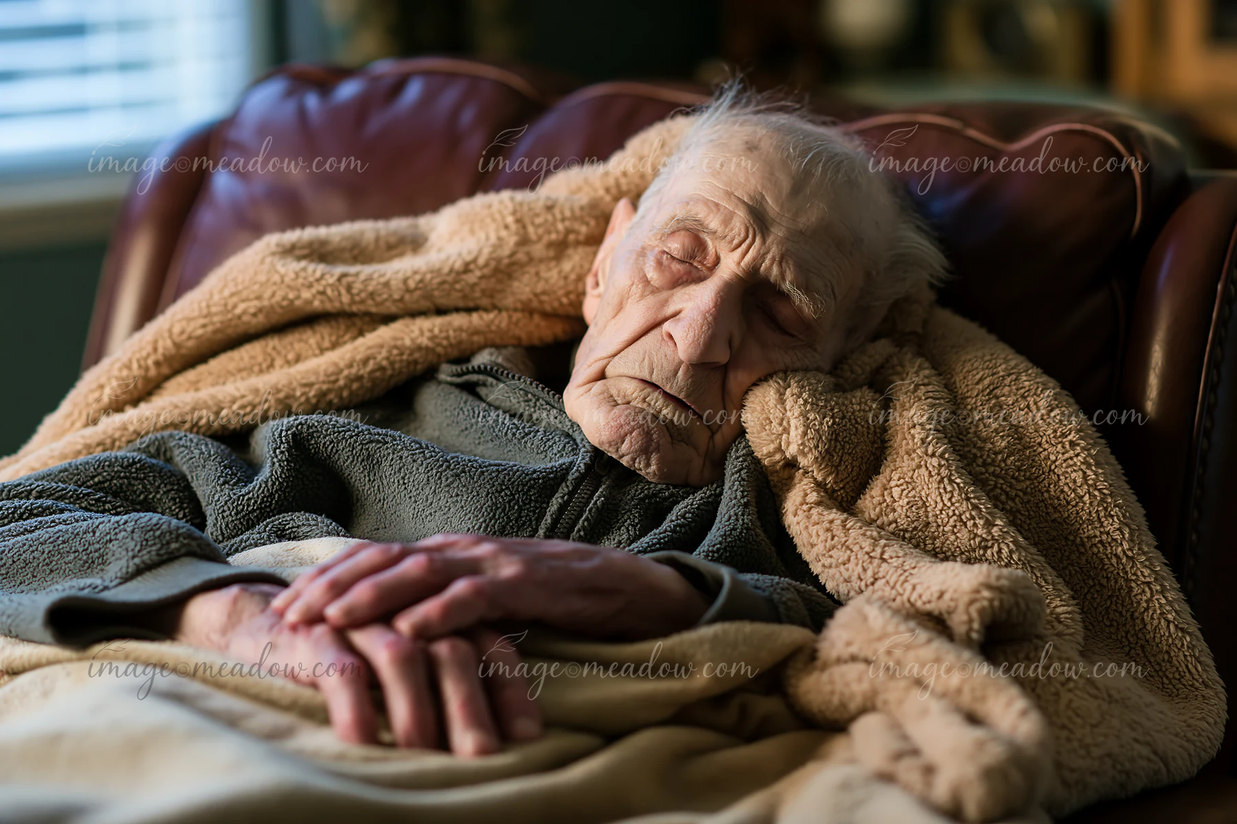 An elderly man with Alzheimer's is resting with a blanket on a chair.