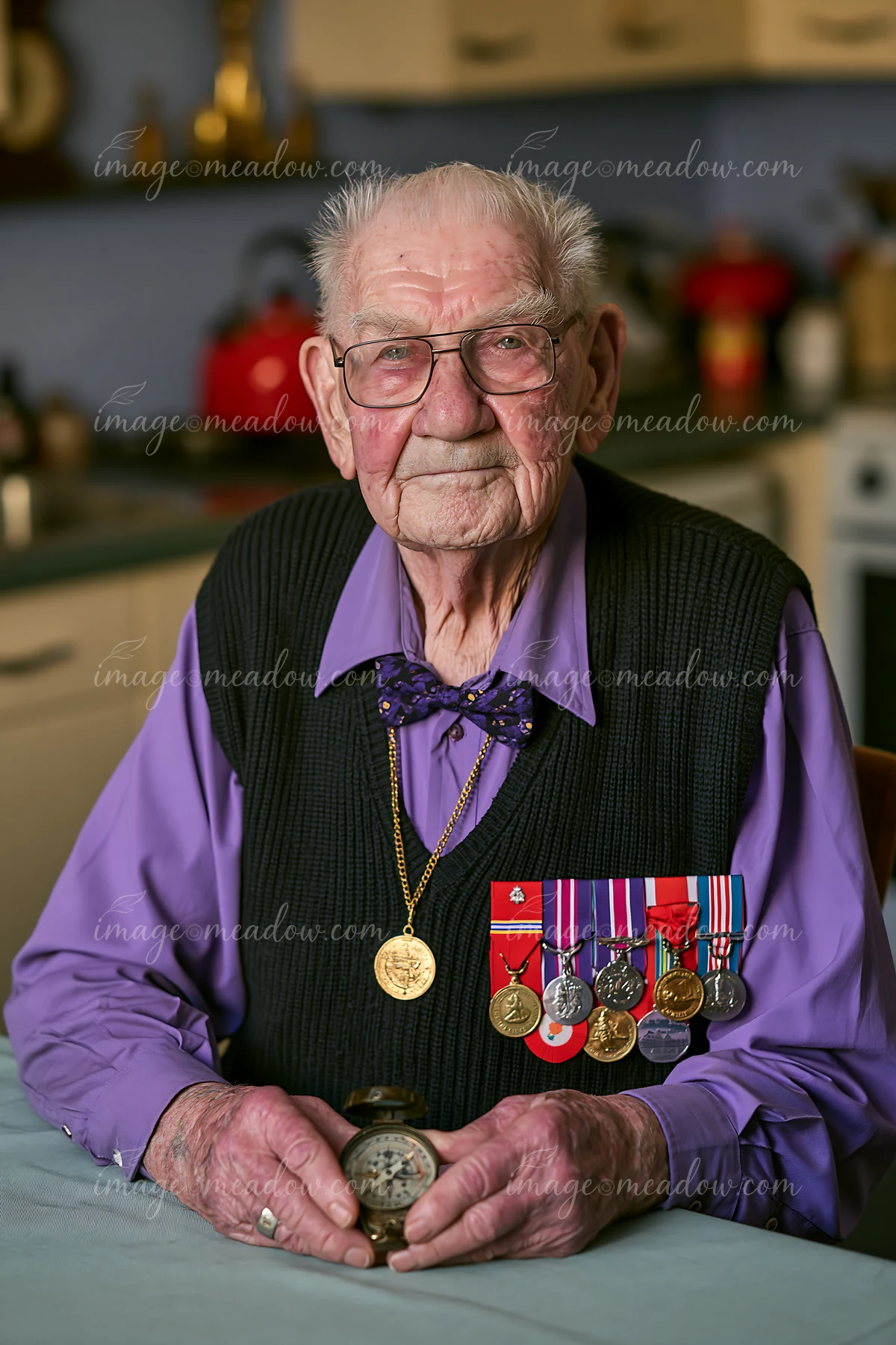 An elderly veteran wearing medals sits at a table inside a kitchen.