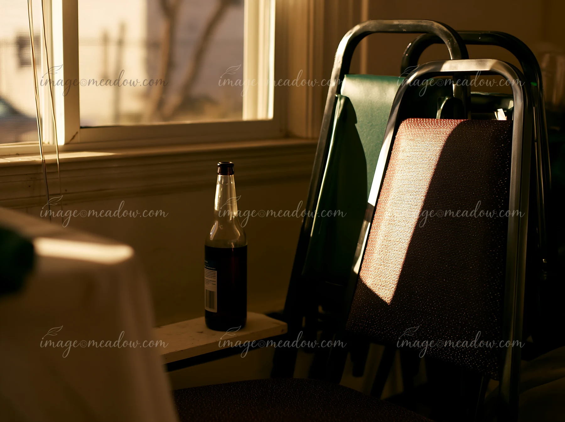 An empty bottle after party sits on a chair in a sunlit room.