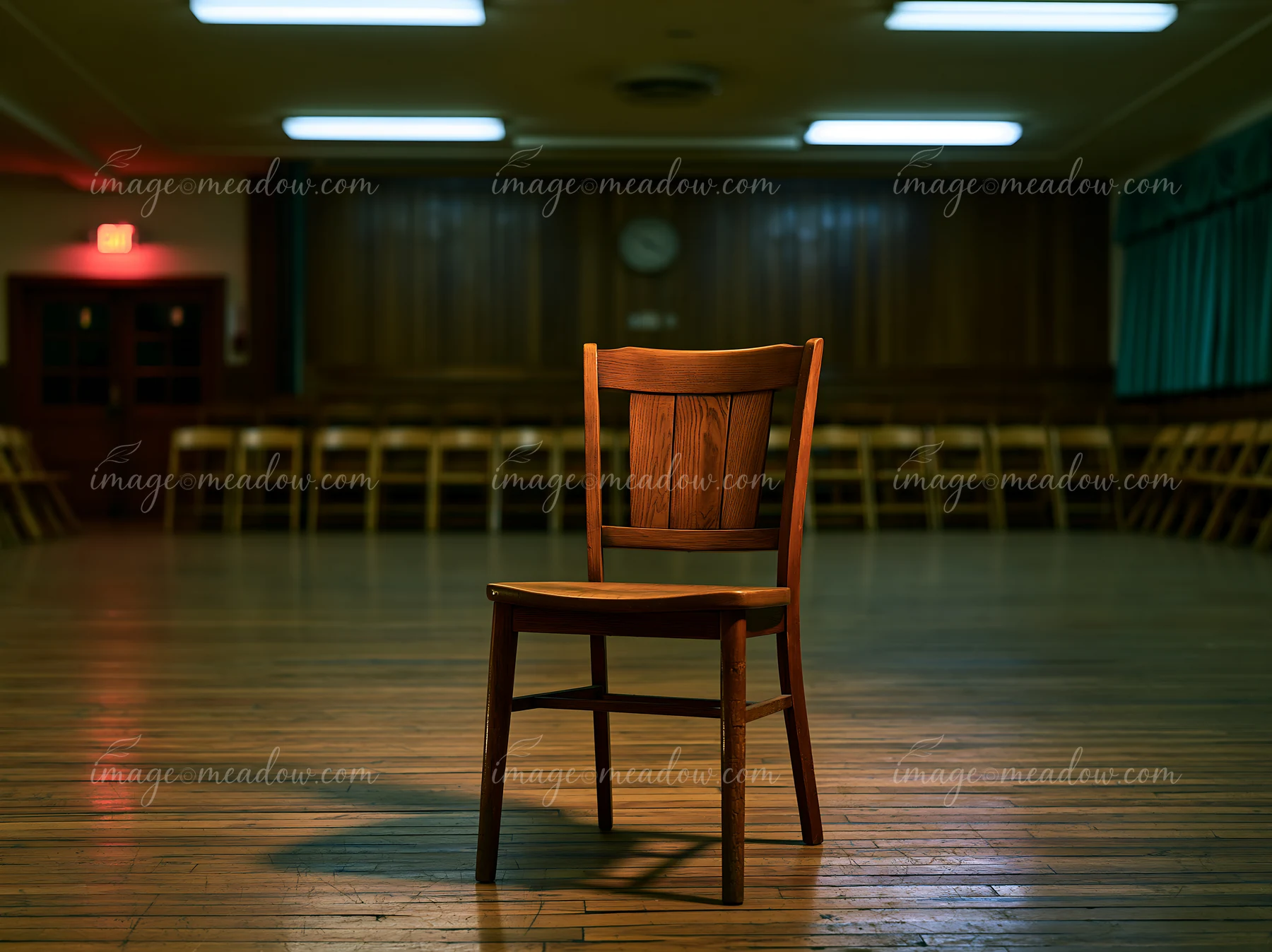 An empty chair stands alone in a dimly lit hall surrounded by rows of chairs.