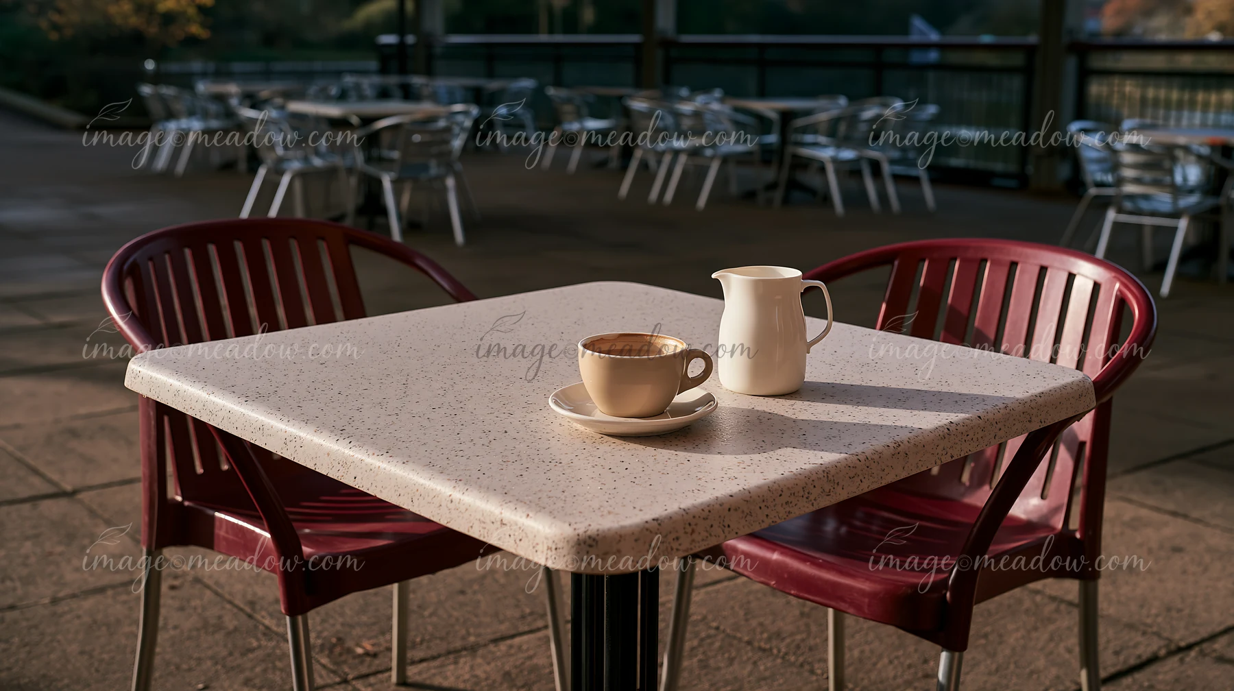 An outdoor cafe table displays a latte and a milk jug.