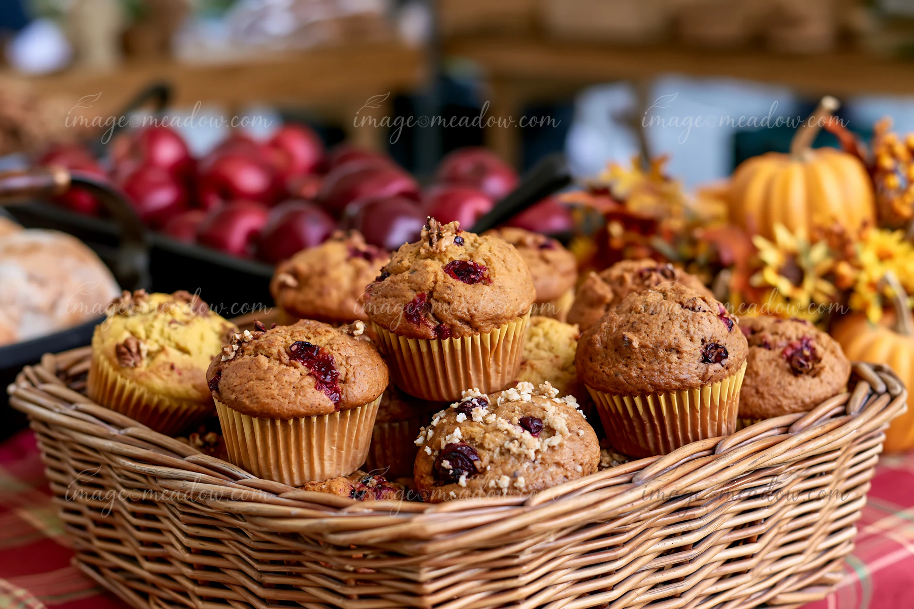 Assorted cranberry and nut muffins fill a woven basket beside pumpkins and autumn foliage.