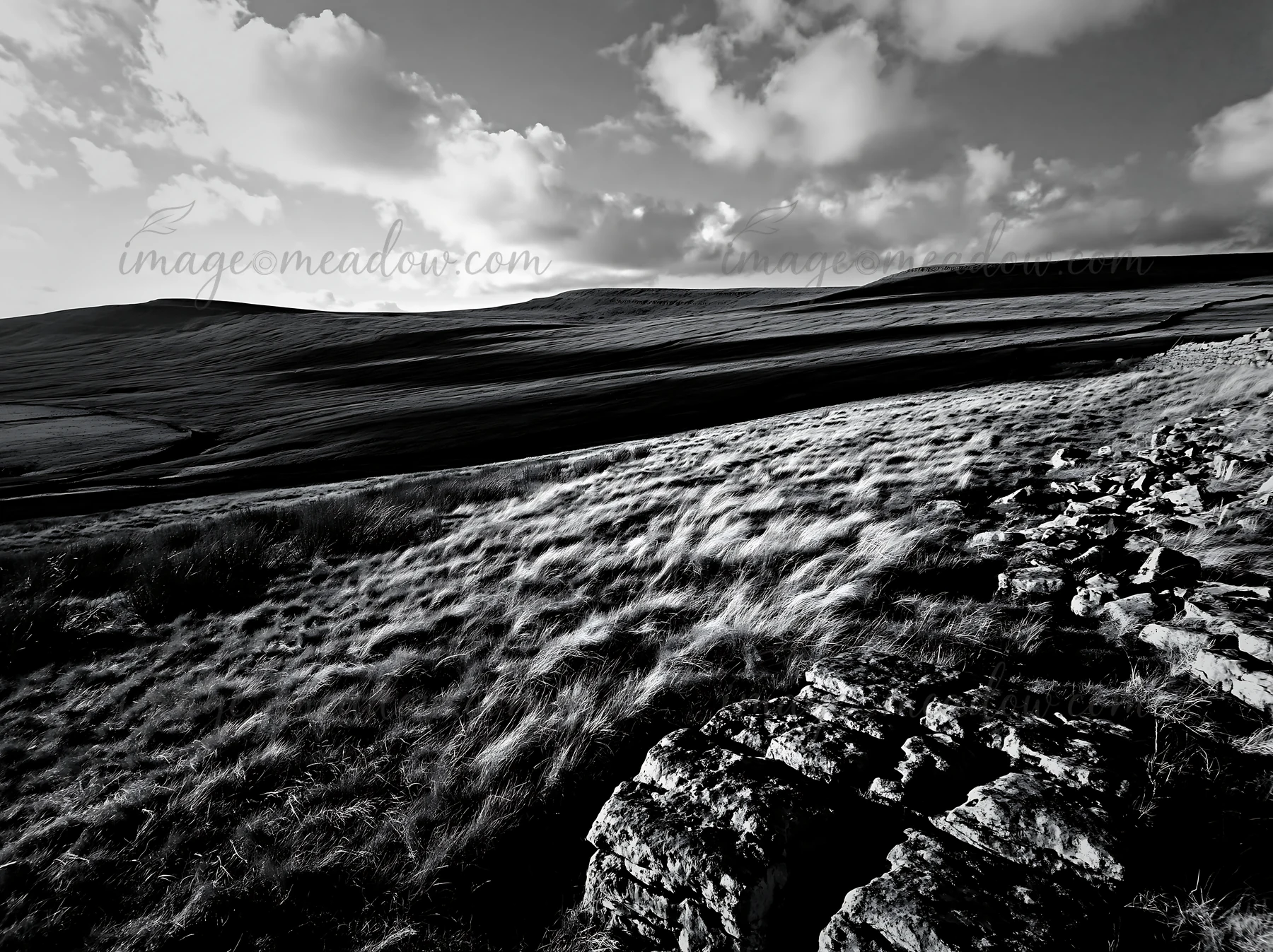 The scene shows an autumn meadow with rocky features in the foreground, set in a hilly area. Clouds fill the sky as shadows cover the landscape, depicting a cal