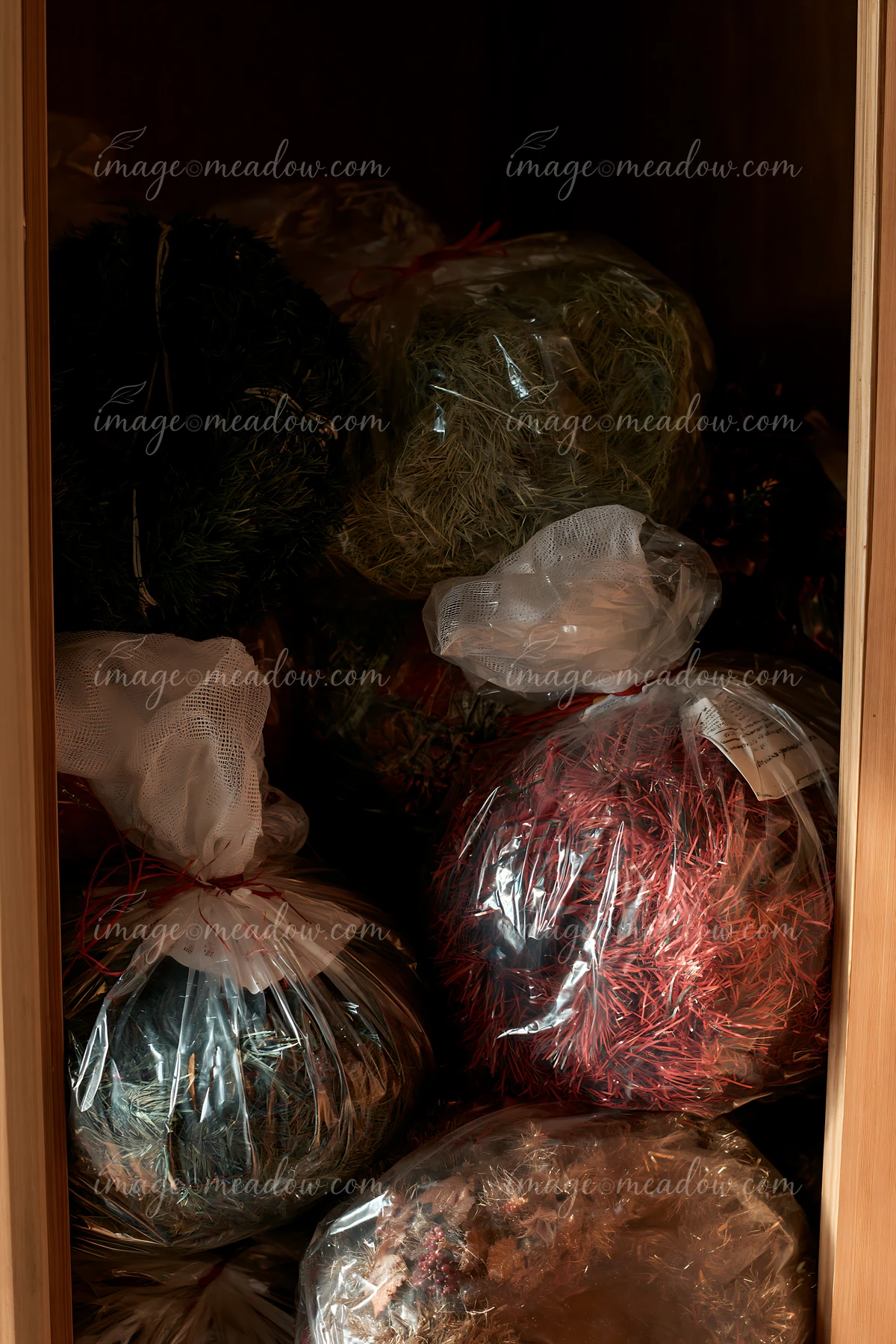 Bagged Christmas greenery and tinsel are packed inside a dark wooden cupboard for storage.