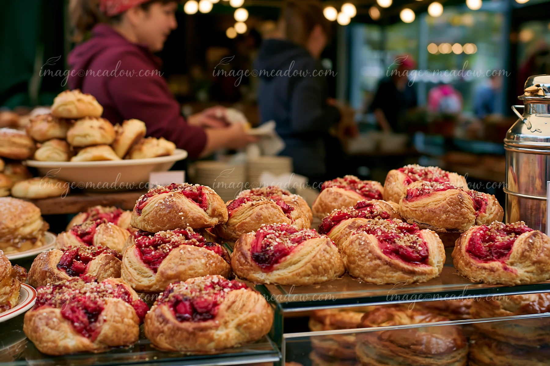 Berry-filled pastries and bread arranged in a glass bakery display with softly blurred customers behind them.