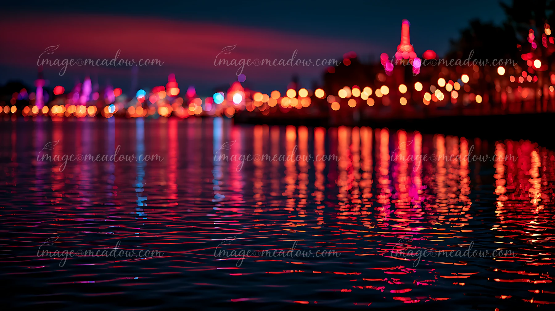 Bright city lights illuminate the waterfront as they reflect in the calm water.