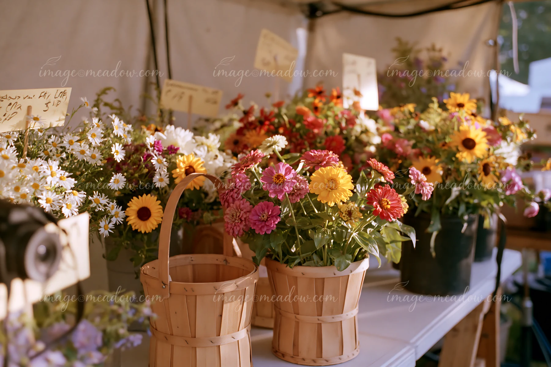 Brightly colored flowers are arranged in wooden baskets at a farmers market.