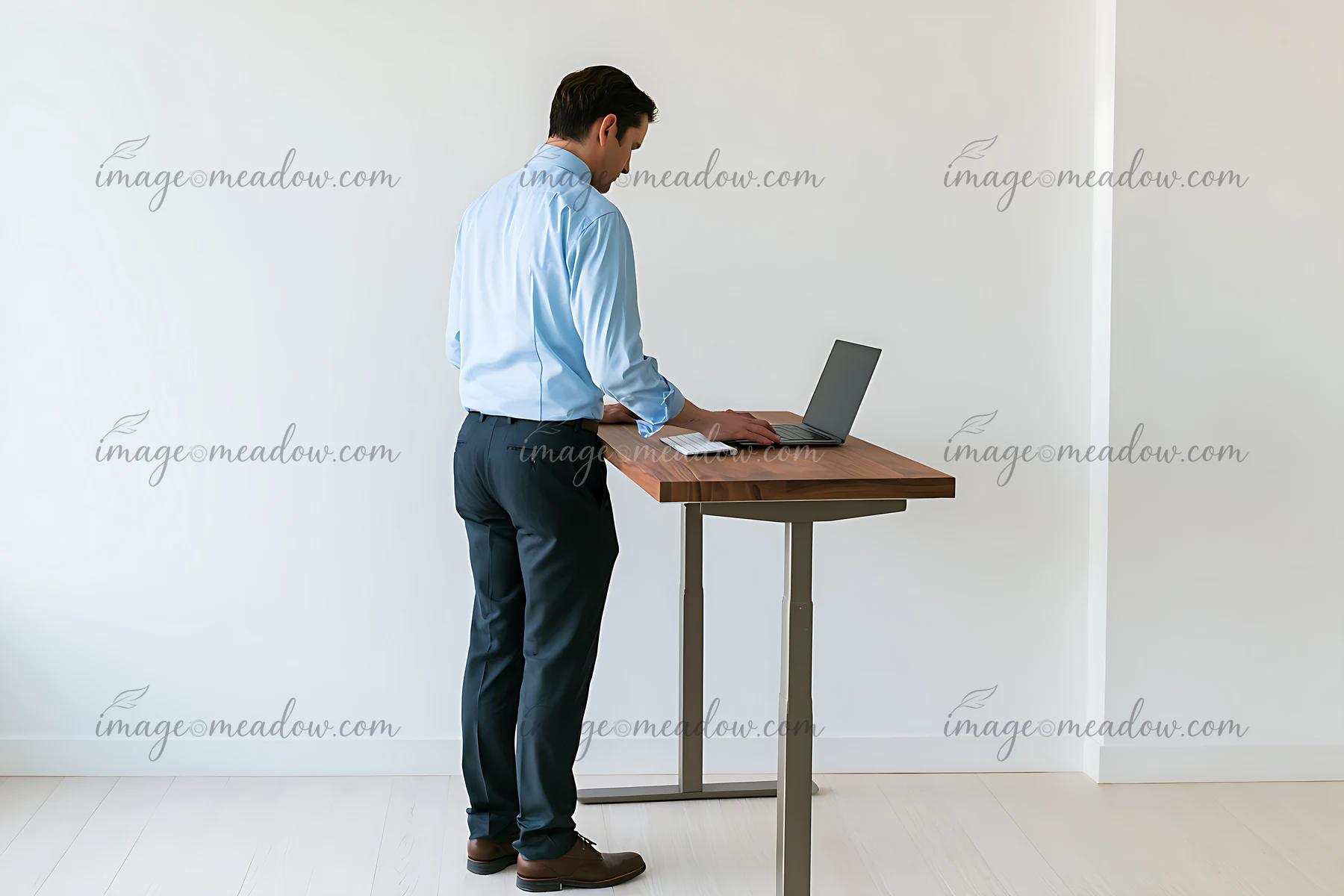 Businessman stands alone at a wooden desk using a laptop in a bright minimalist office.