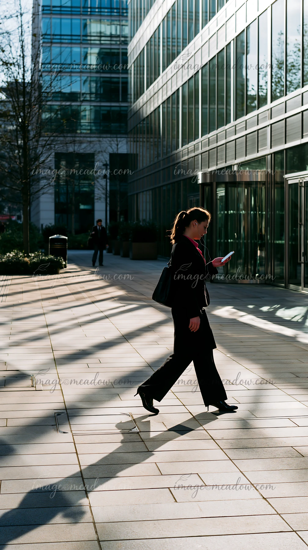 Businesswoman walks outside a modern glass office building while looking at her smartphone.