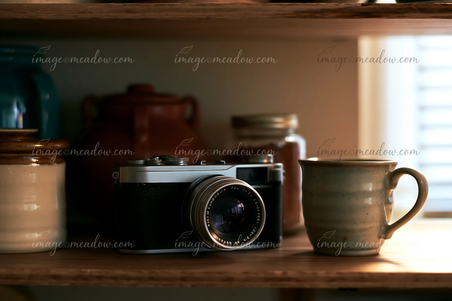 Camera and lens on a wooden shelf sit alongside a ceramic cup and various jars.