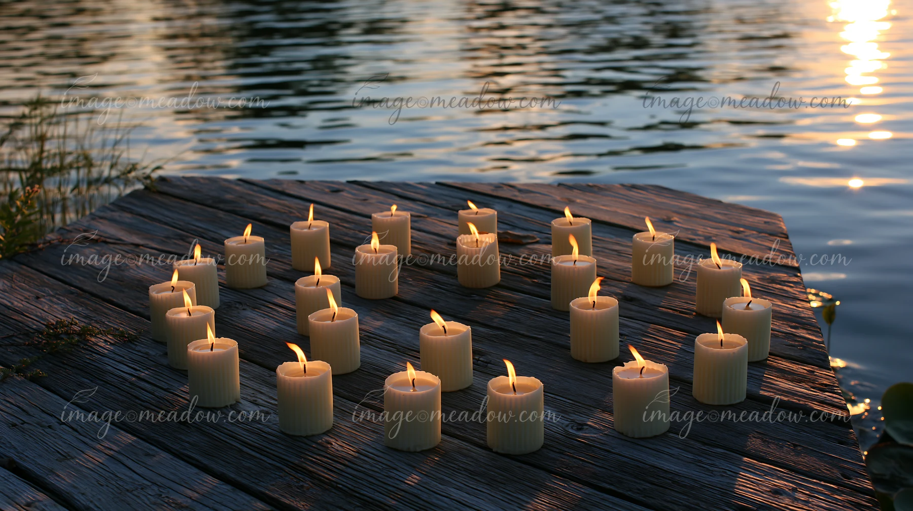 Candles arranged in a circle sit on a wooden platform next to the water.