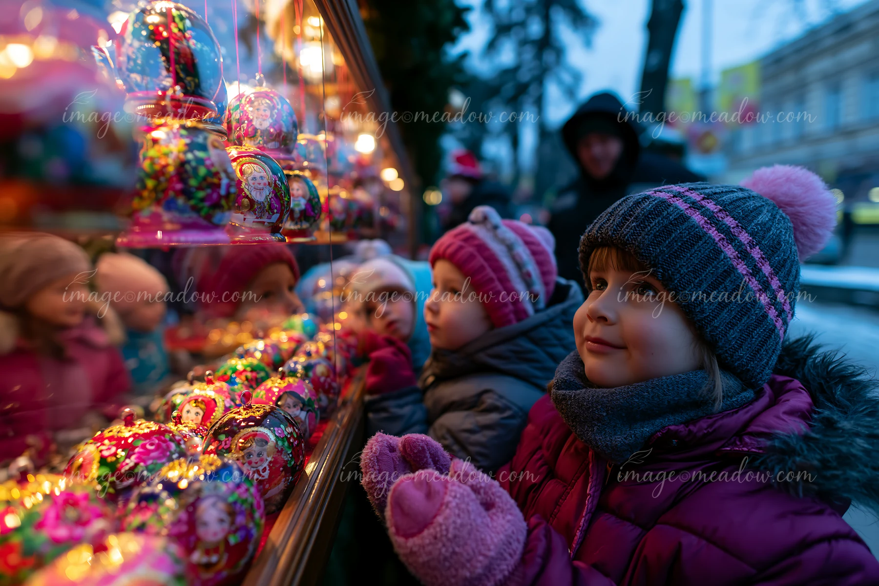 Children are looking at handmade ornaments displayed at a Christmas market stall during the evening.