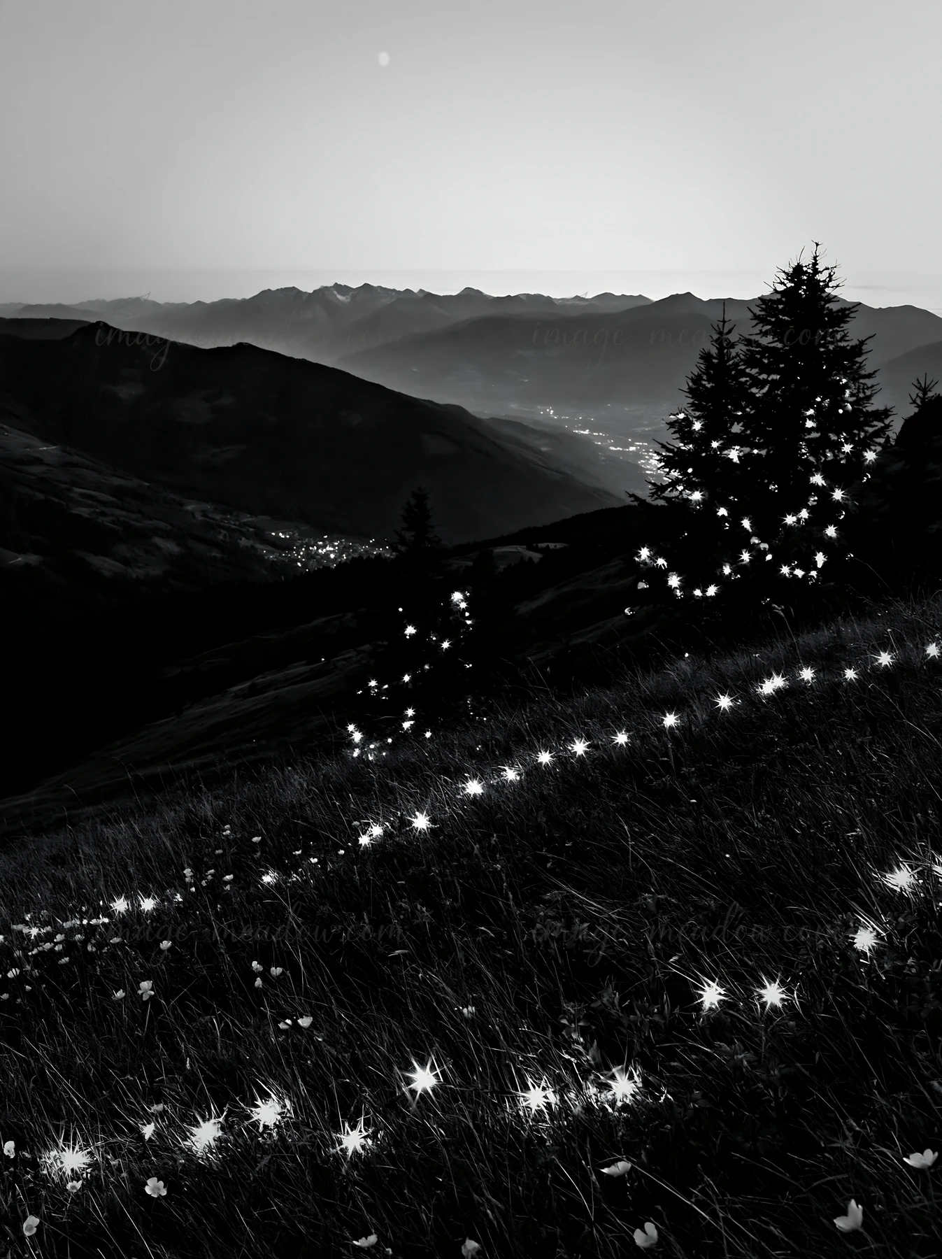 Bright lights shine across a deep mountain valley meadow during Christmas. The landscape offers a view of distant mountains and a valley below, all in the eveni